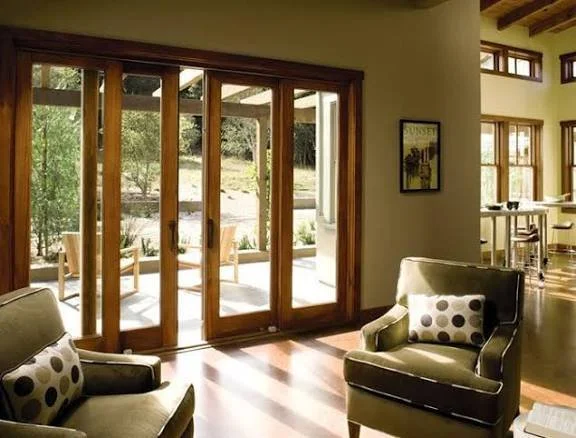 Living room with wooden-framed sliding glass doors leading to an outdoor patio, with two armchairs and polka dot cushions, and a picture on the wall.