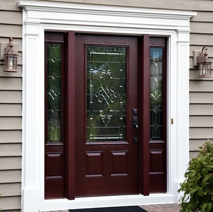 Front door with glass panel and decorative glass design, surrounded by white trim, with beige siding on the house exterior and outdoor lantern lights on each side.