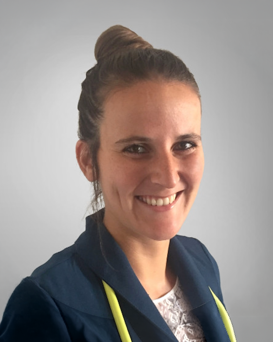 Portrait of a woman with brown hair tied in a bun, smiling, wearing a navy jacket with yellow accents, against a plain gray background.