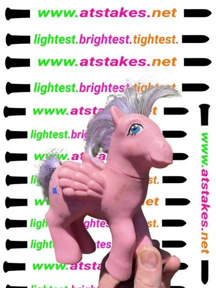 A pink plastic unicorn toy with a gray mane and a blue star on its front leg, held in front of a mugshot-style background with repeated colorful text and a height measurement scale.