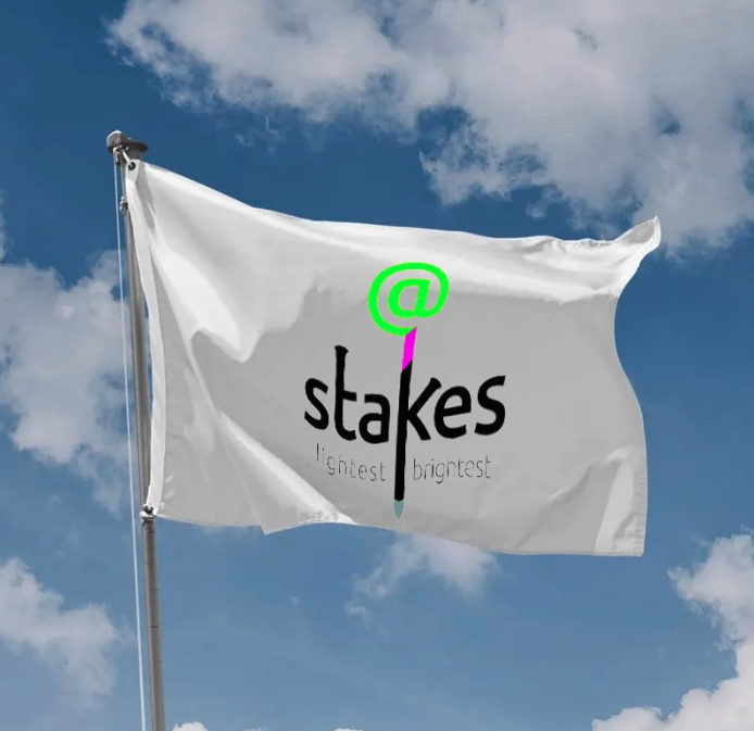 A white flag with a logo and text, flying in the sky with clouds. The logo features an at symbol '@' in green, a black ink pen, and the word 'stakes' in black. Below it, in smaller gray text, are the words 'brightest' repeated twice.