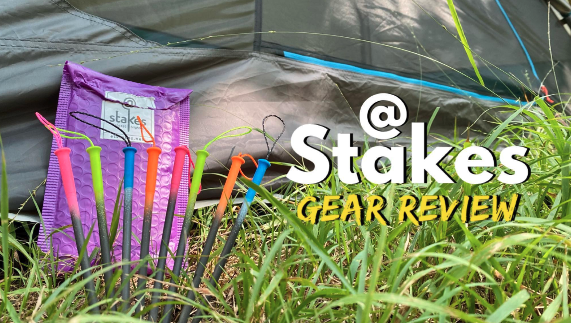A set of colorful stakes with different colored tips in grass, near a purple carrying case, with a background of a gray tarp and some grass.