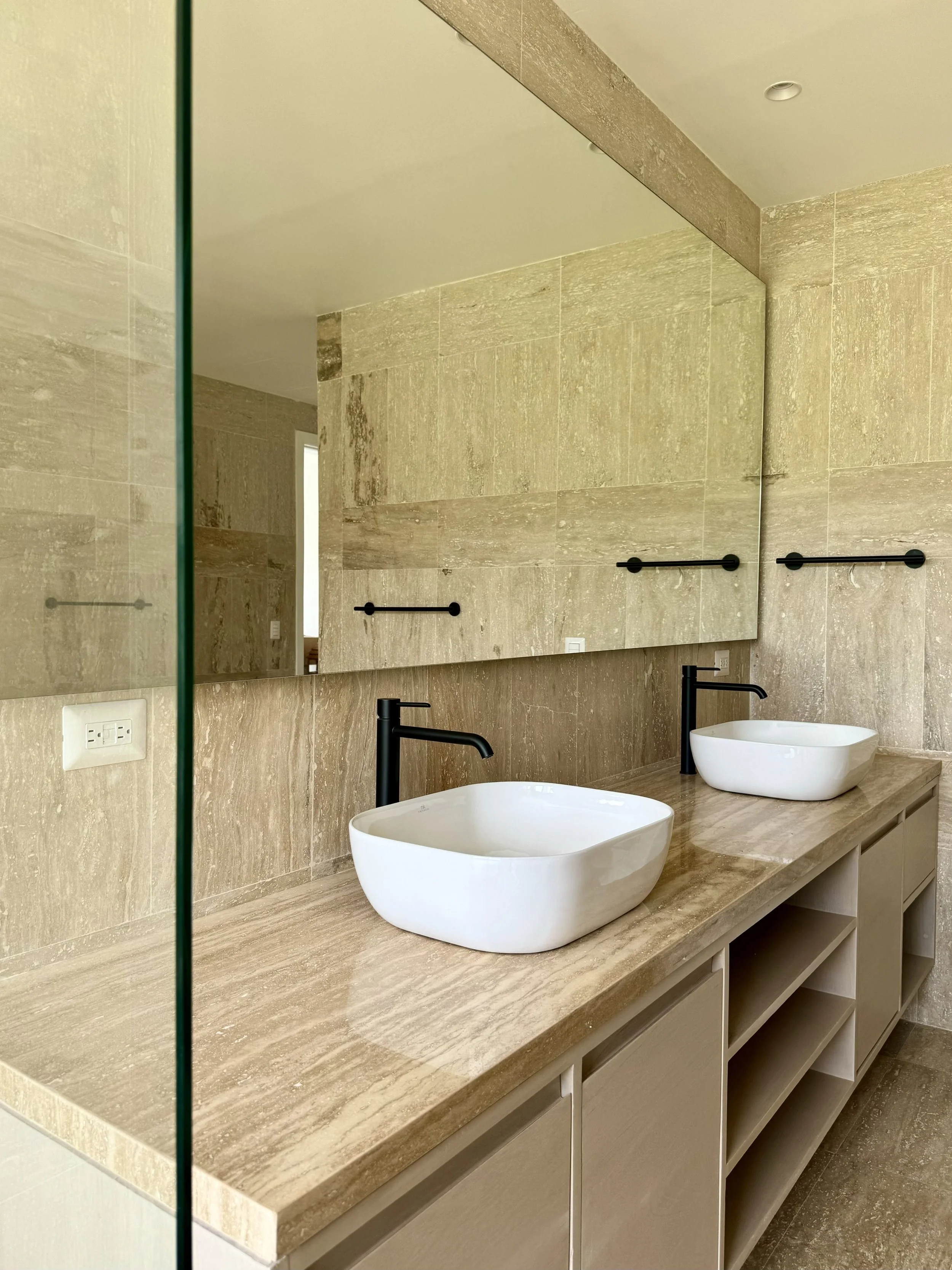 Primary bathroom of a completed private residence in Casa de Campo, designed and sold by Yamilis de la Rosa and built by Constructora Caña Roja, featuring natural stone, custom cabinetry, and matte black fixtures.