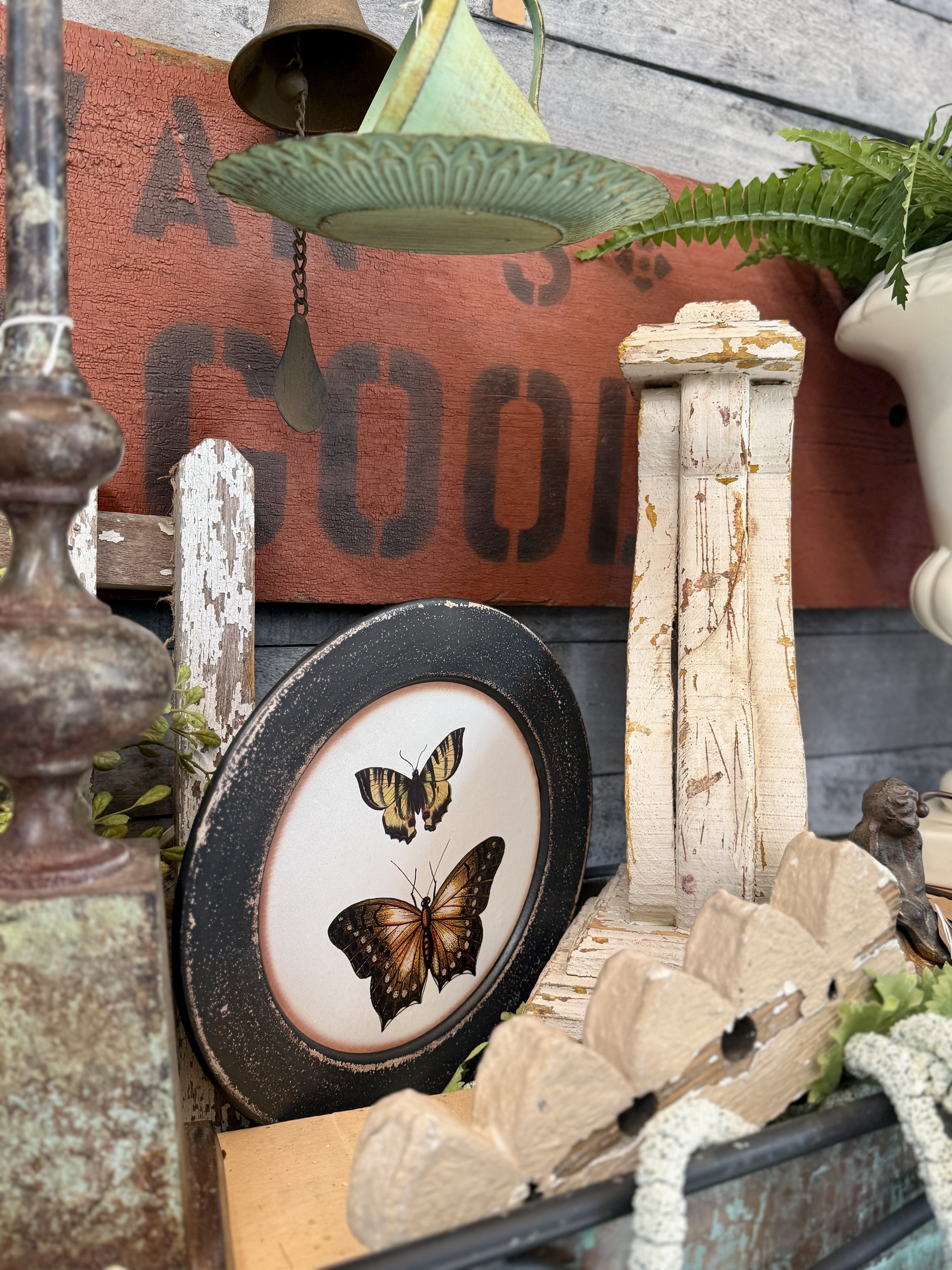 Decorative arrangement with vintage items, including a framed butterfly illustration, weathered wooden pieces, and metal objects, set against a rustic red painted wall.