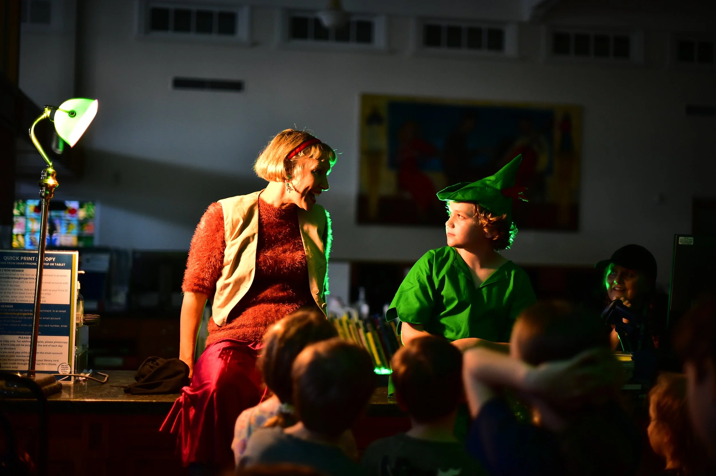A woman with short hair and a red headband is talking to a young child dressed as Peter Pan. This show was created for the Cairns Children's Festival and was called Night at the Library.