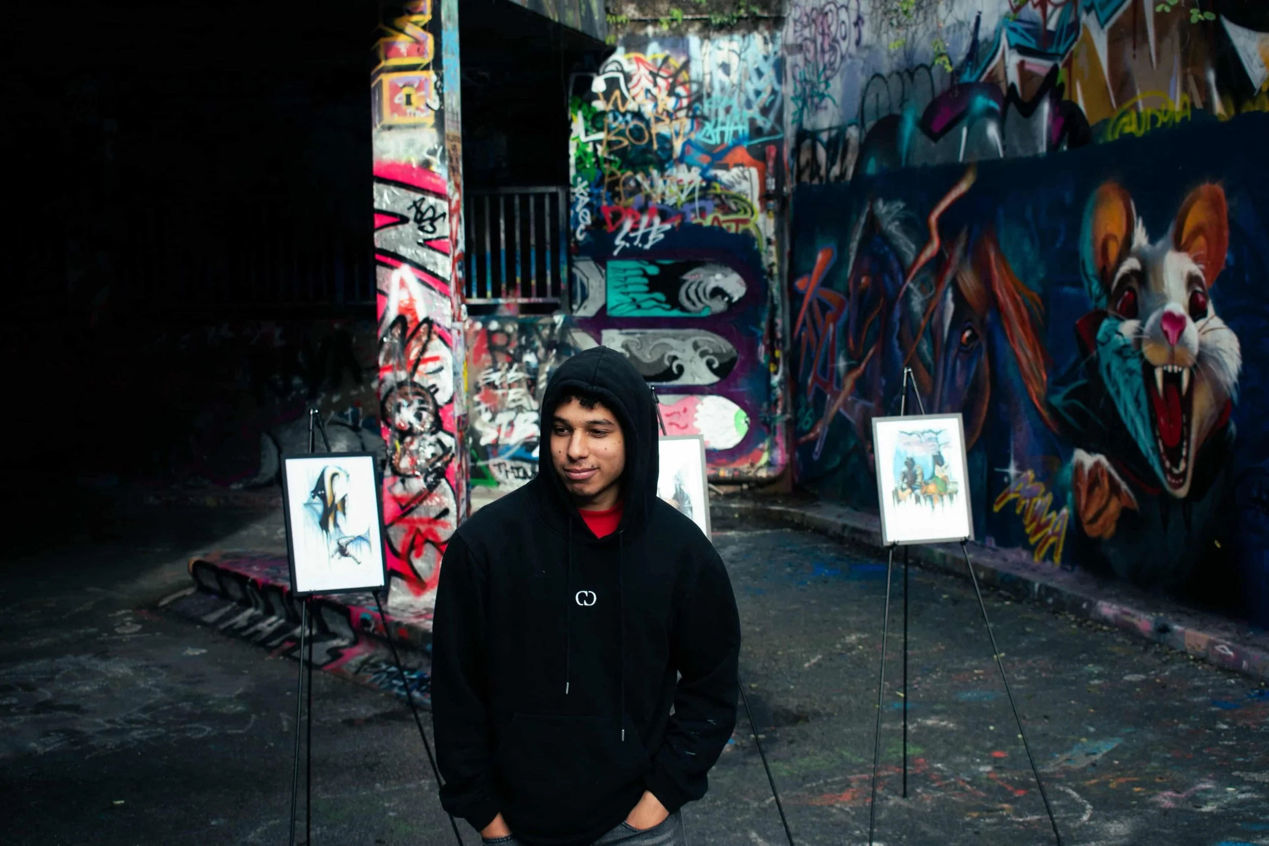 Mysterious hoodie figure standing with his artwork in graffiti environment.