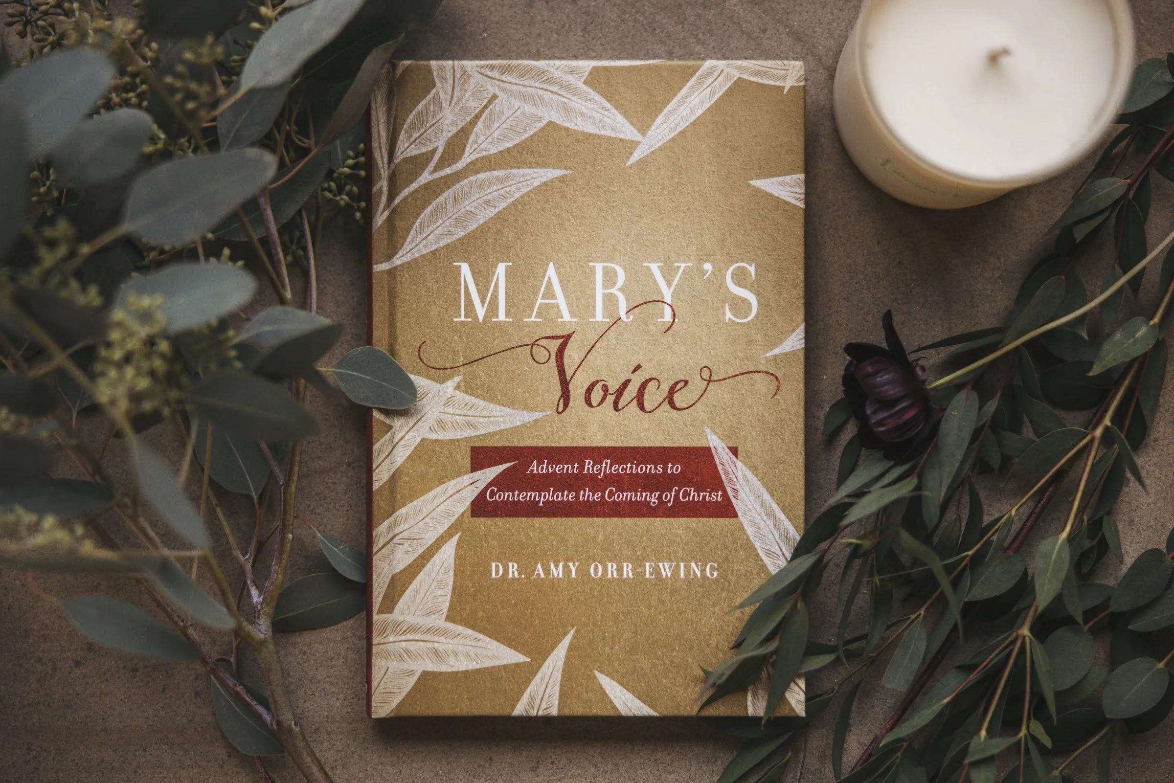 Mary's Voice by Dr Amy Orr-Ewing, laid on a wooden table among eucalyptus with a lit candle