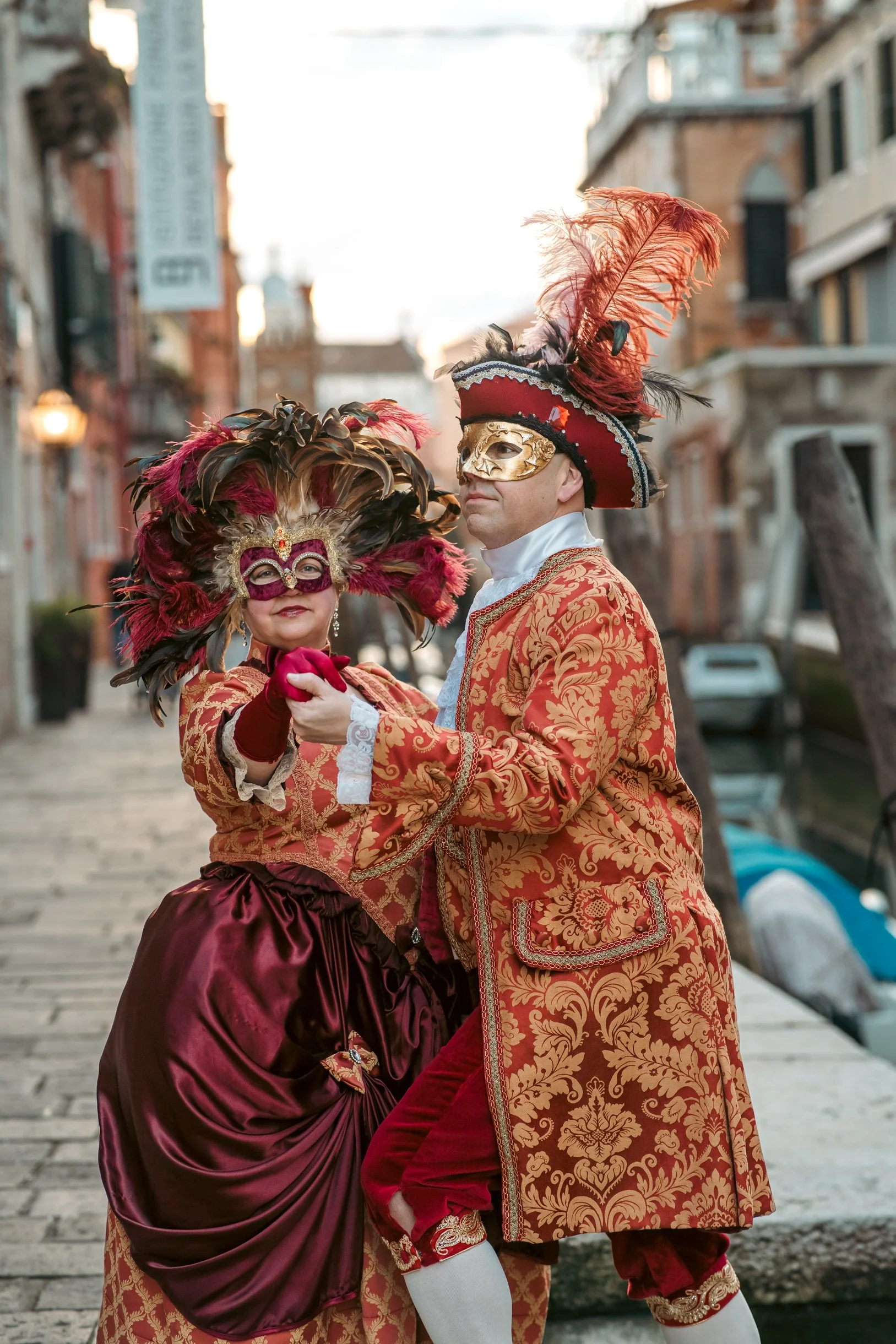 Two people in venitian historical costumes dancing on an outdoor street at sunset. 