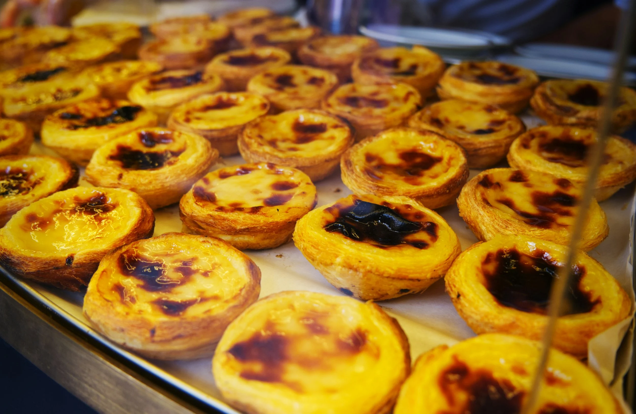 Close-up of multiple Portuguese egg tarts, some with caramelized tops, arranged on a tray.