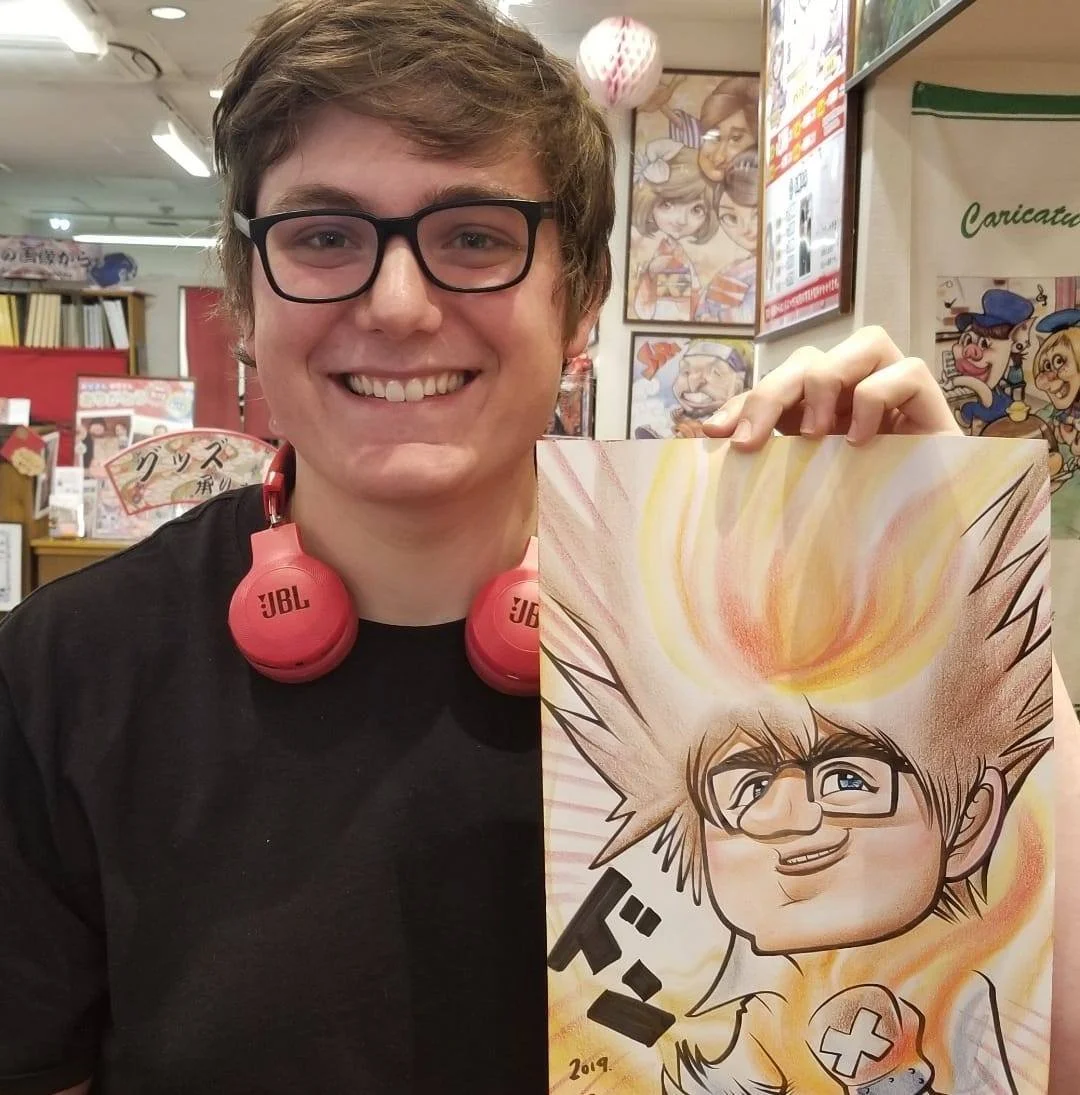 Smiling person with glasses holding a colorful cartoon drawing of themselves, with spiky hair and flames on their head, in a store filled with artwork and posters.