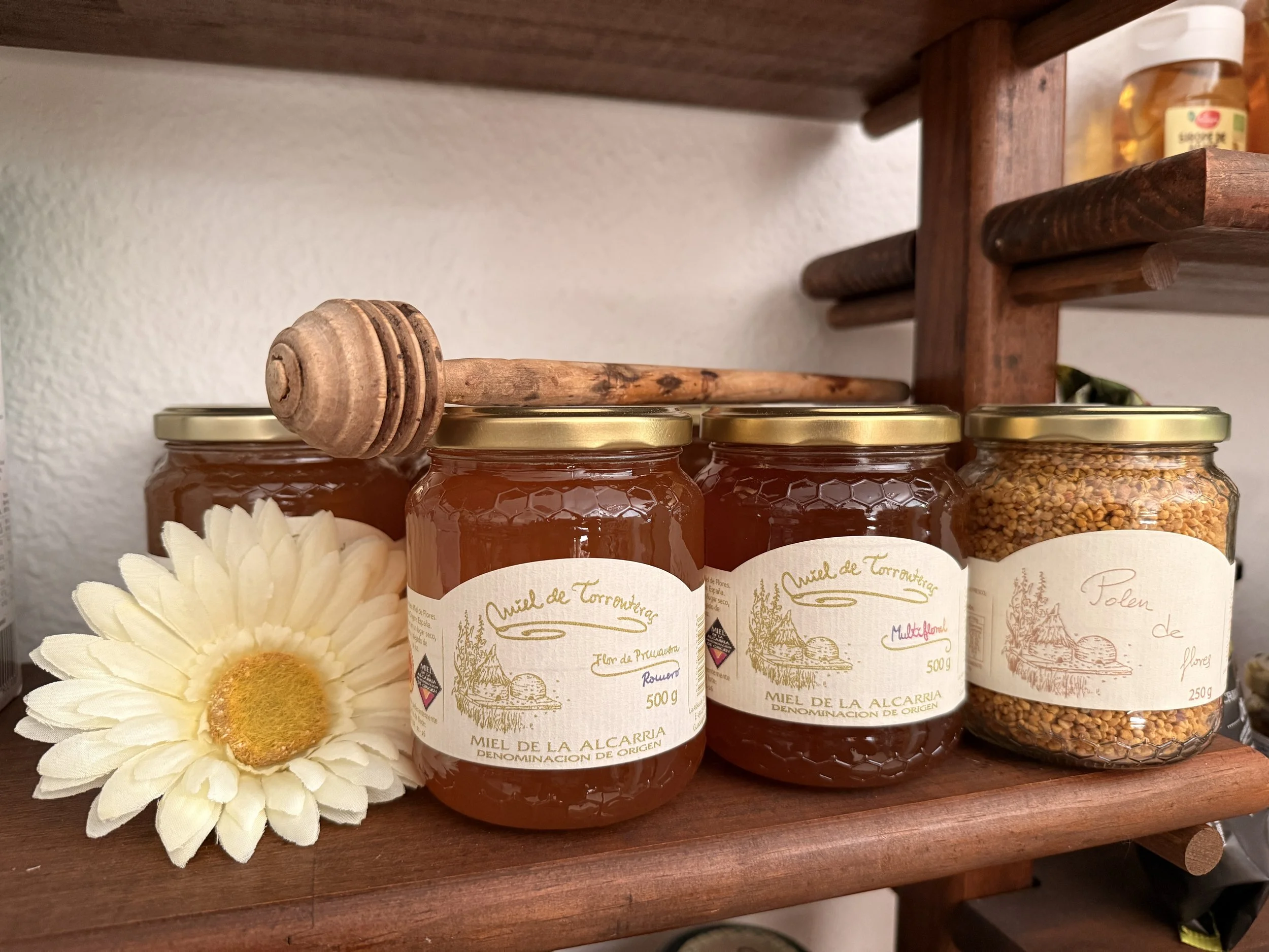Tarros de miel de abeja con etiquetas en un estante de madera y una flor blanca junto a ellos. Miel de la zona de la Alcarria. 