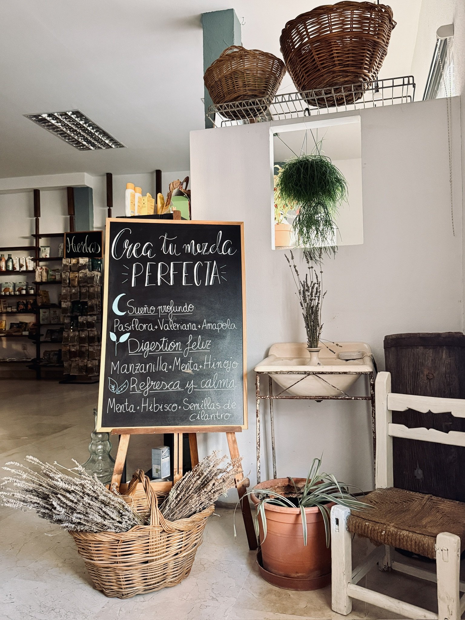 Interior de azahar herbolario tienda con una pizarra de buen tamaño que invita a crear mezclas perfectas con ingredientes naturales, acompañada de cestos y plantas decorativas. En Sacedón, España.