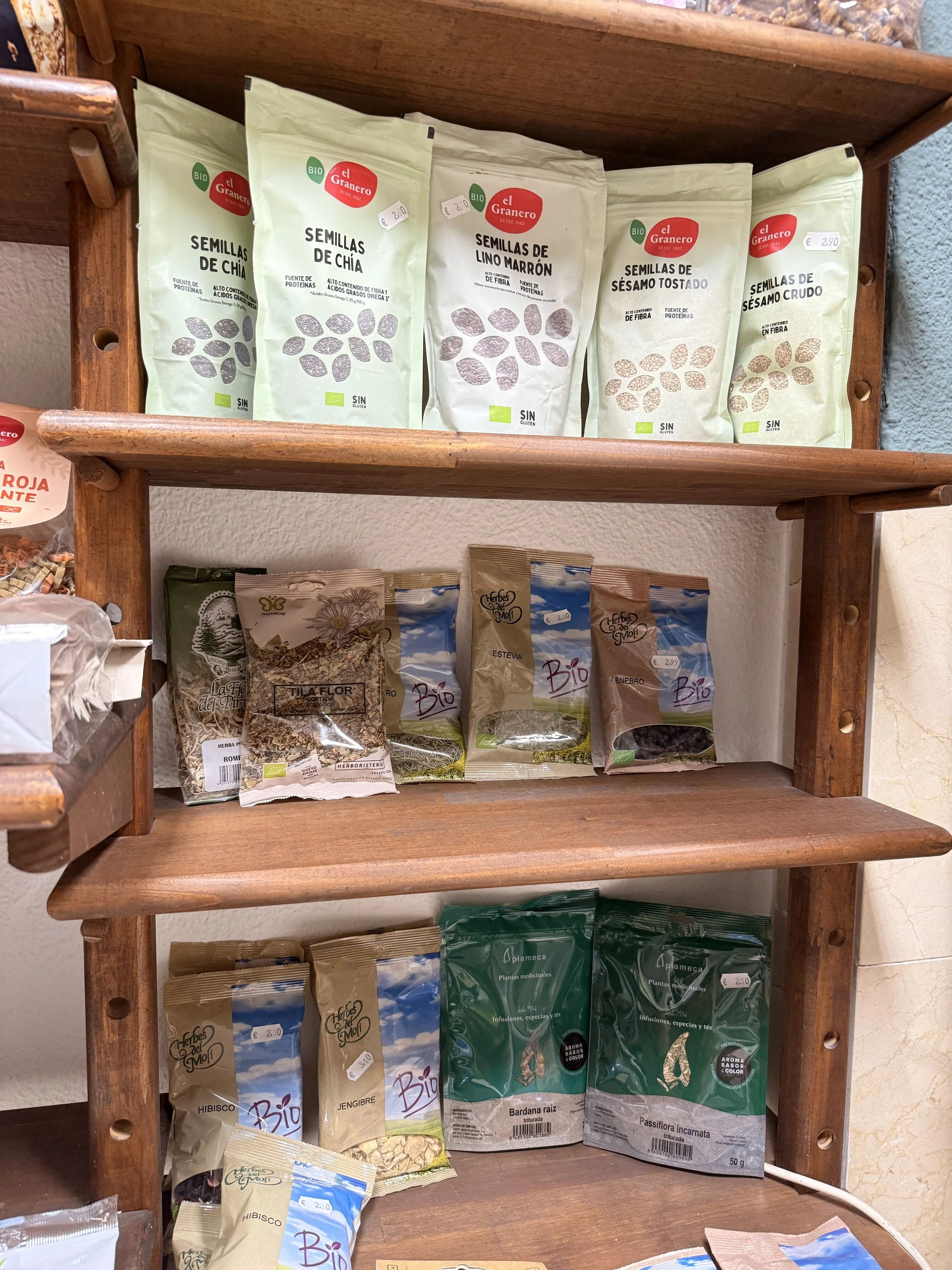 Variedad de paquetes de semillas y hierbas medicinales en una estantería de madera en una tienda natural o herbolario.