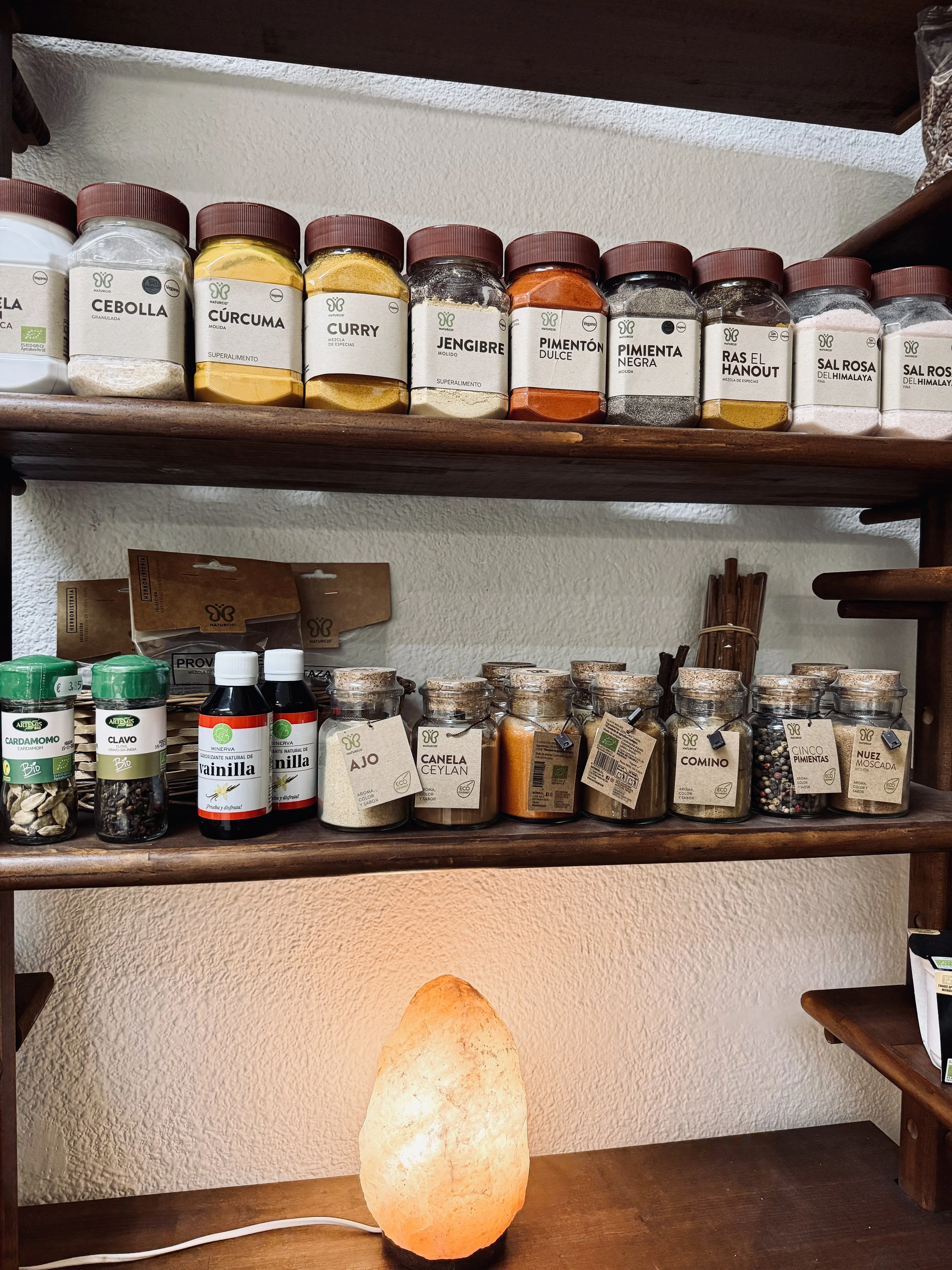 Estante con especias en frascos y saleros de sal rosa y sal del Himalaya, lámpara de sal en una mesa de madera.