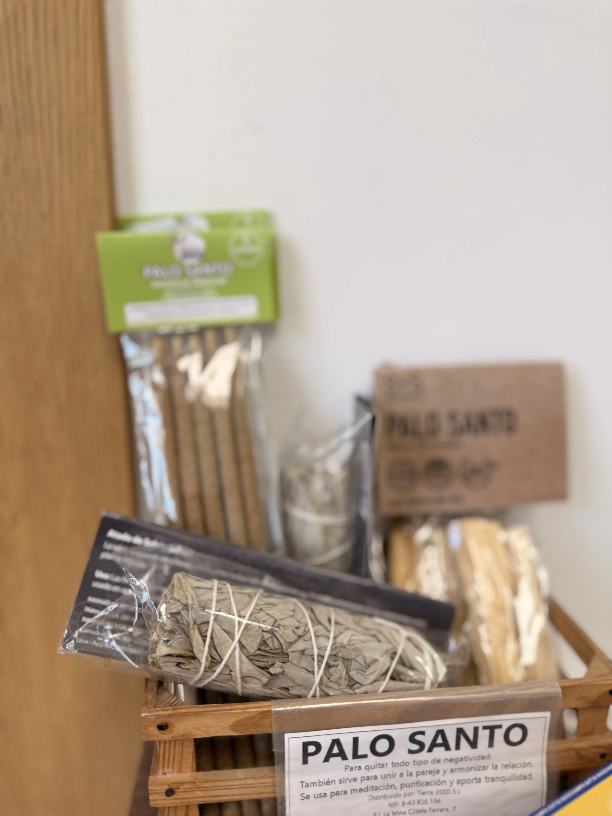 Palo Santo en una tienda, en una caja de madera con una etiqueta que dice 'PALO SANTO' en letras grandes y una descripción en español sobre sus usos y beneficios.