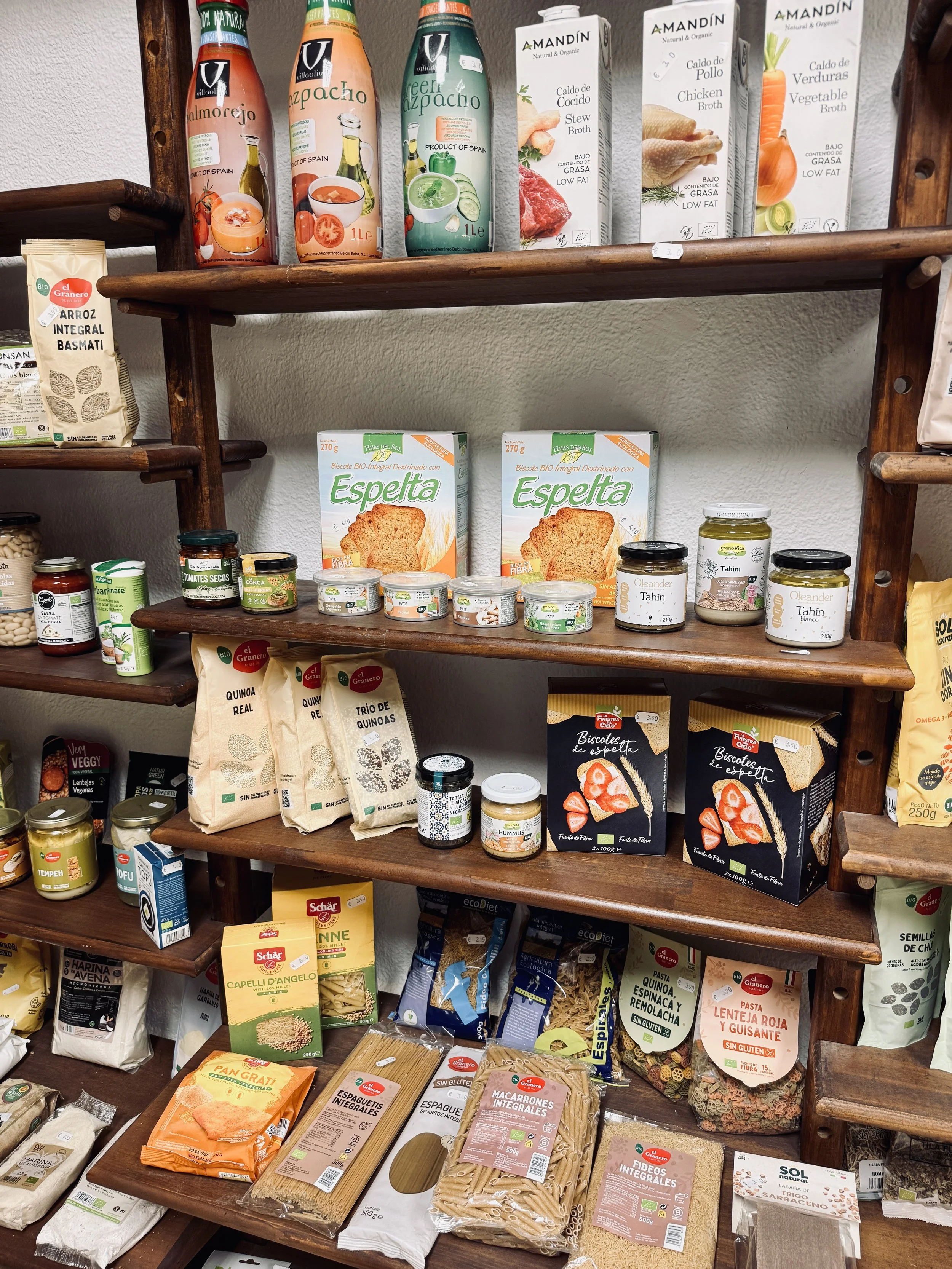 Estantes con productos orgánicos y naturales como caldos, jugos, galletas integrales, pasta, legumbres, tahini, hummus y otros alimentos en envases de cartón, vidrio y plástico.