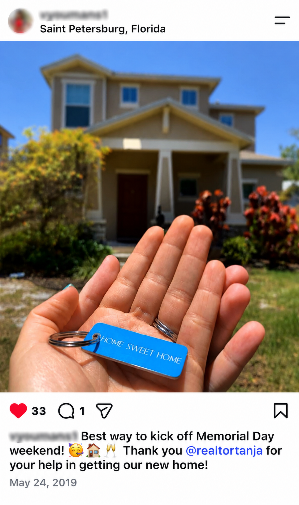 Hand holding a keychain with a blue tag that says 'HOME SWEET HOME' in front of a house in Saint Petersburg, Florida, with plants and trees in the yard, and a blue sky above.
