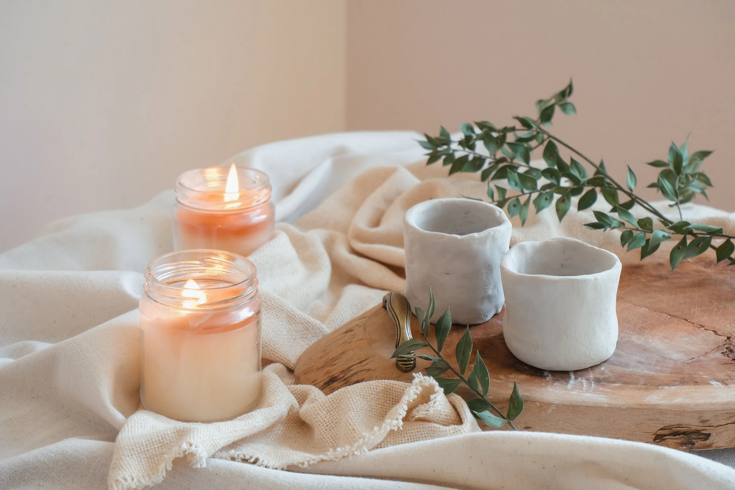 Candles, cups and greenery arranged on soft natural fabrics