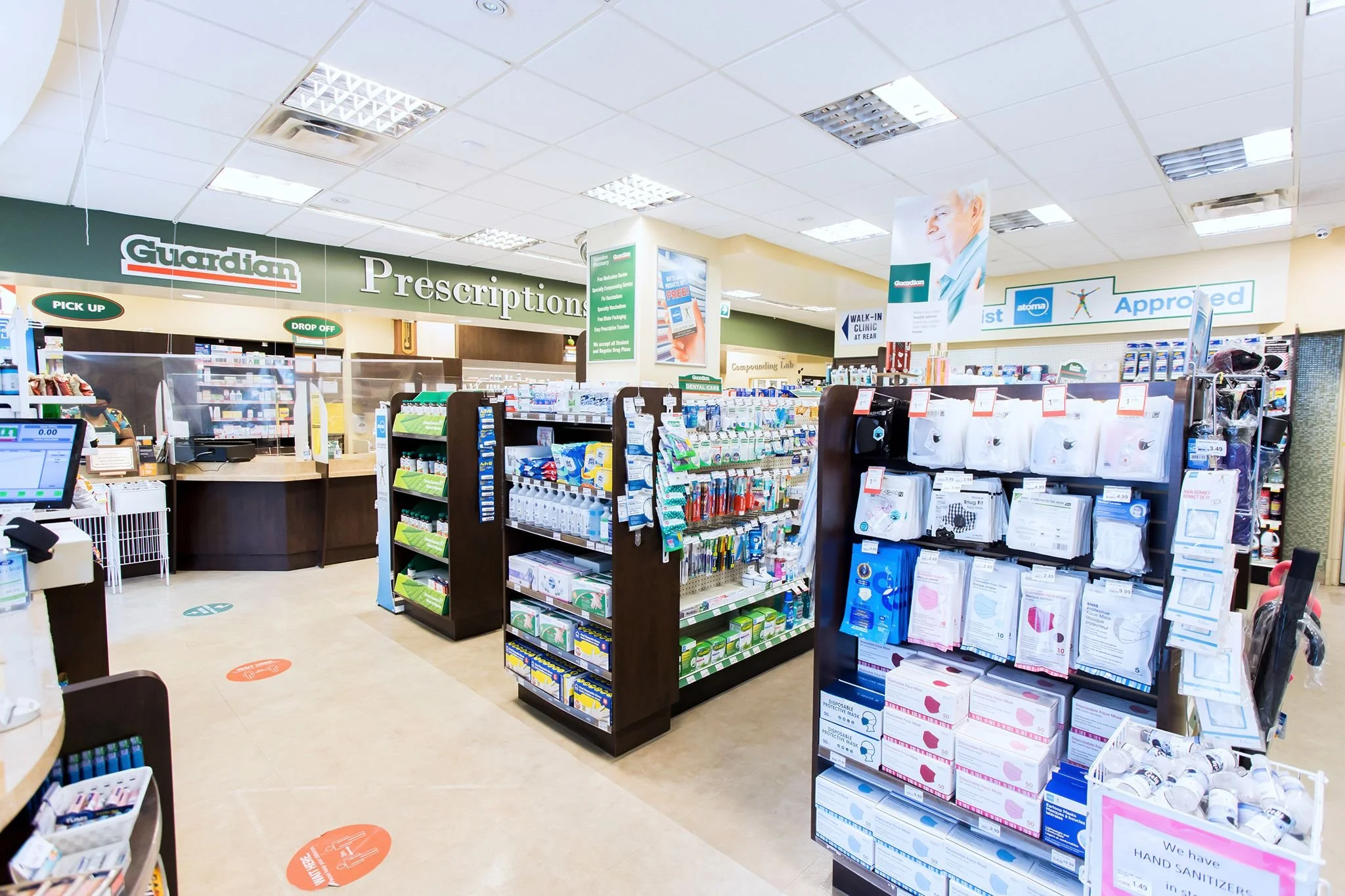 Inside a pharmacy showing the prescription counter, shelves with health and personal care products, and signs indicating pick-up and drop-off areas.