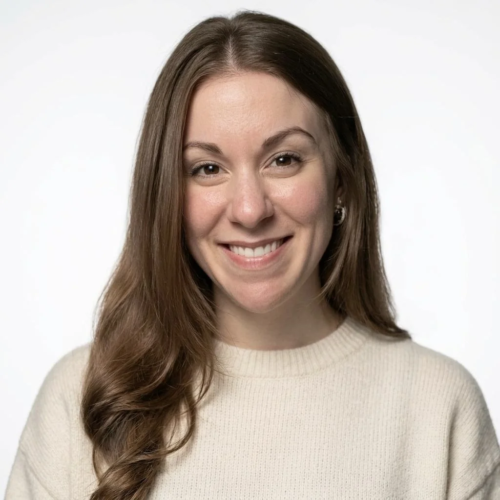 A direct headshot of Lindsey, a brown-eyed, medium brown haired woman. She is smiling with her hair down, tucked behind her shoulder on the left side.