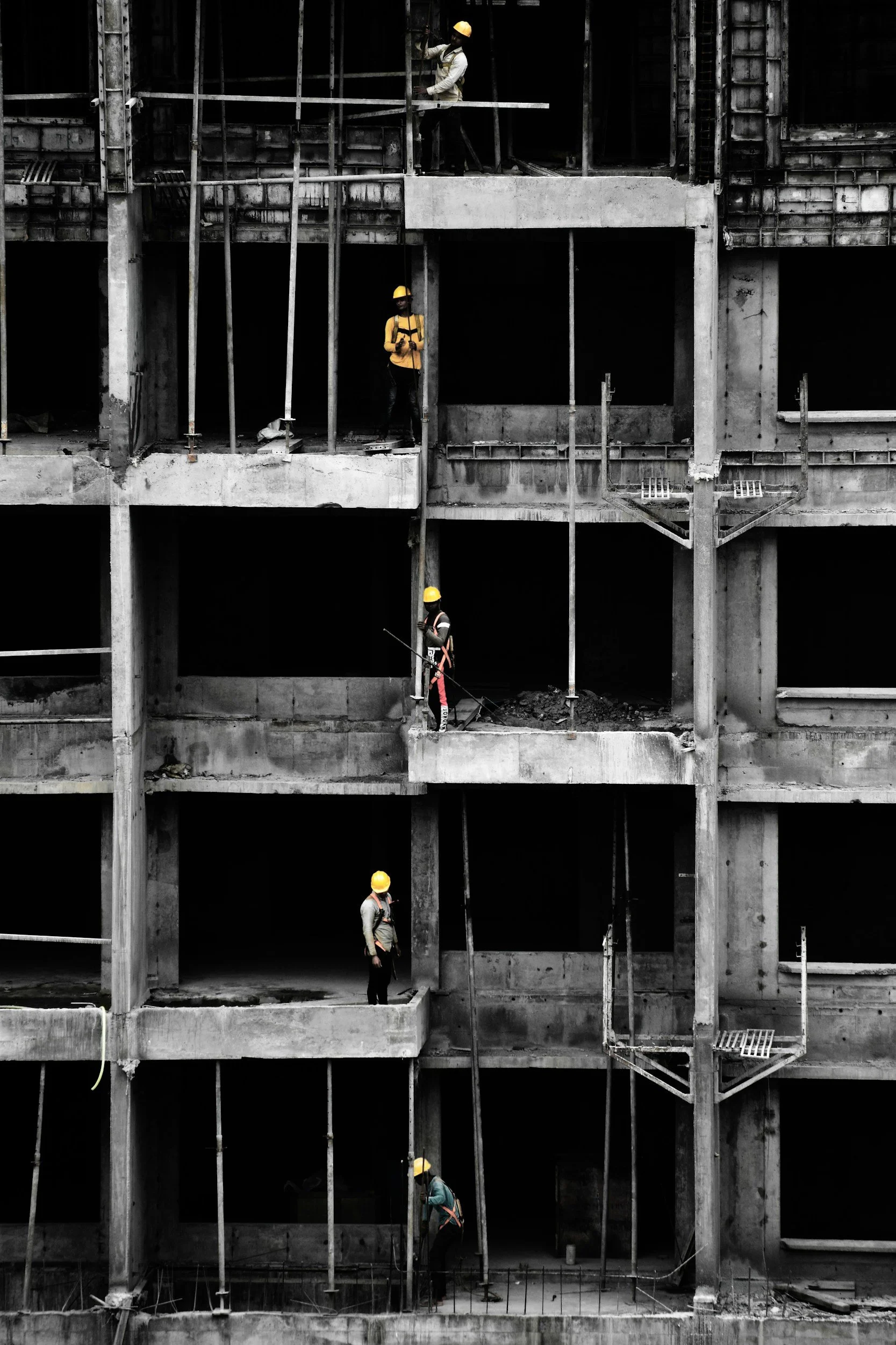 Construction workers with yellow hard hats working on the framework of a multi-story building under construction.