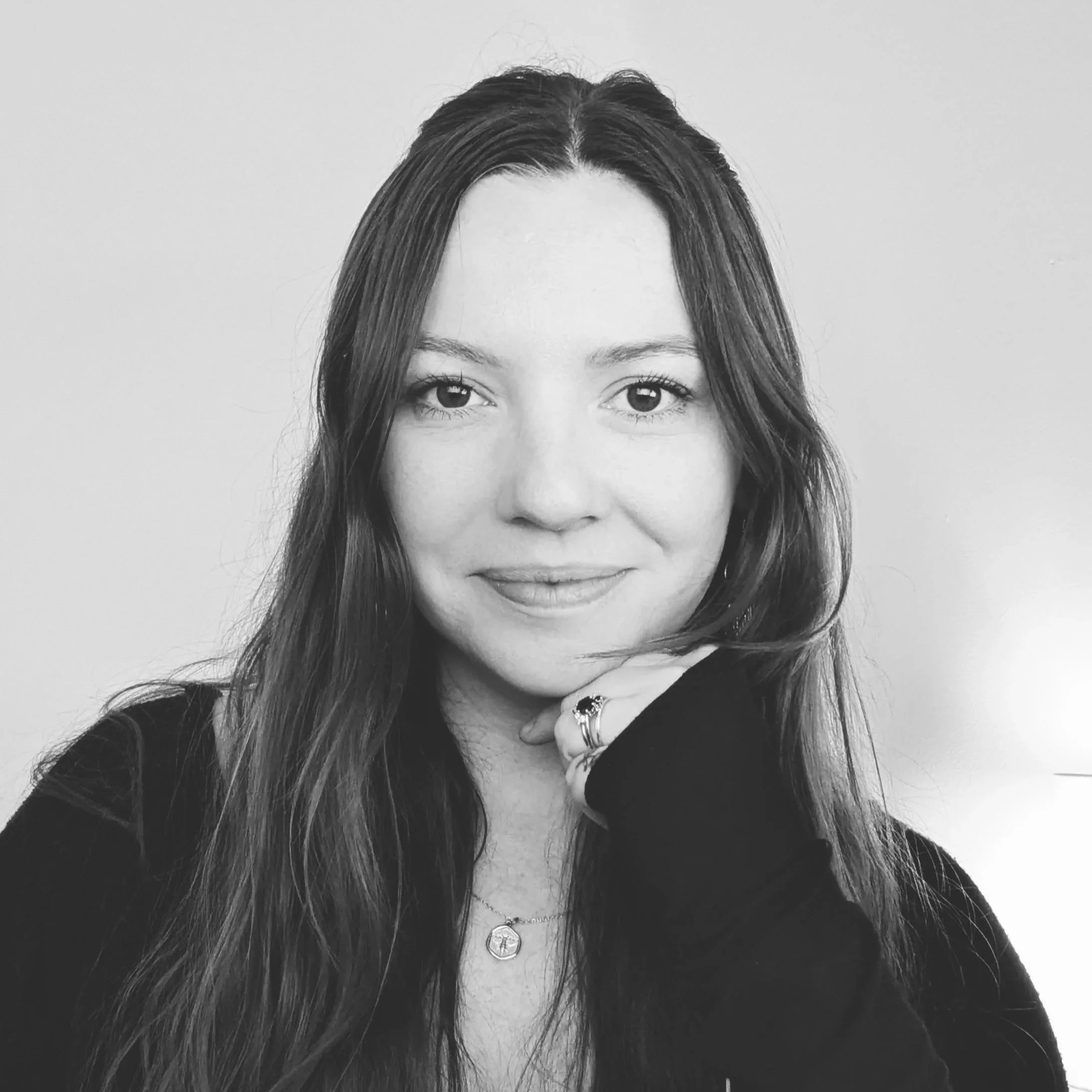 Black and white portrait of a woman with long hair, wearing a dark top, and jewelry including rings and necklaces, smiling softly.