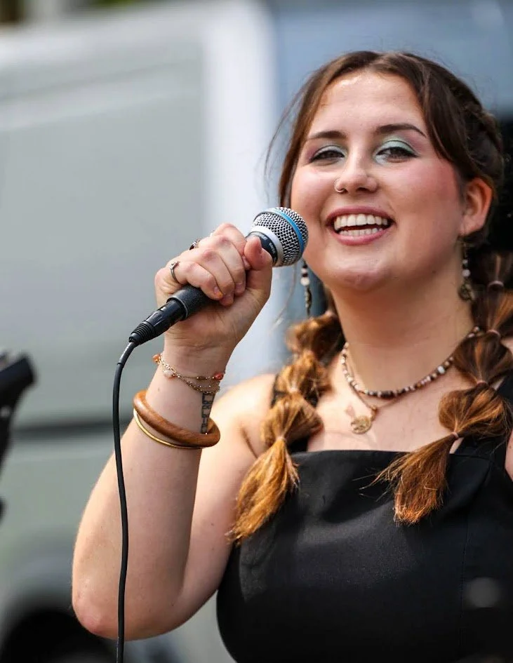 A young woman with braided hair holding a microphone and smiling at the camera.
