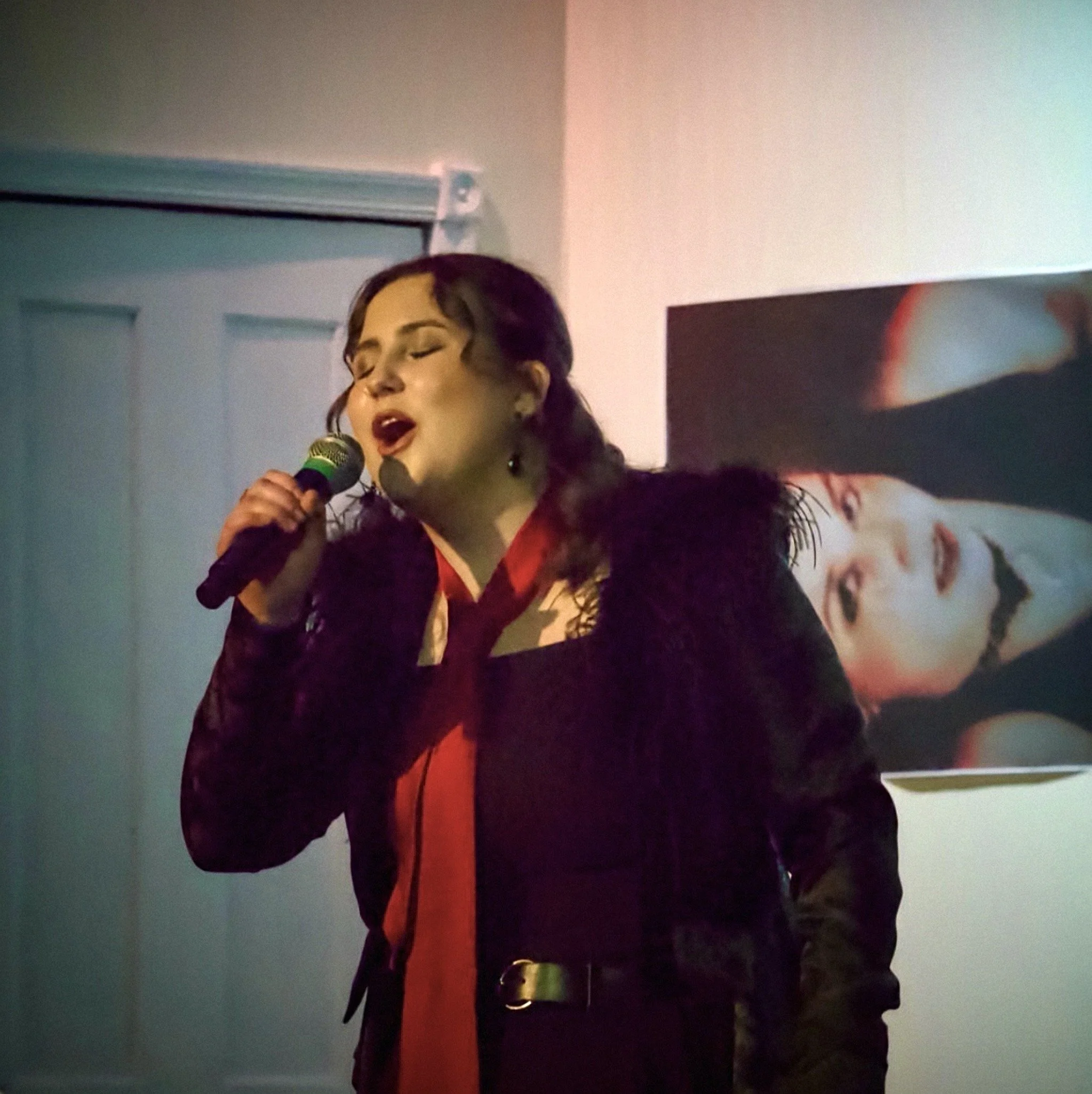 Woman singing into a microphone in a dimly lit room with colorful lights.