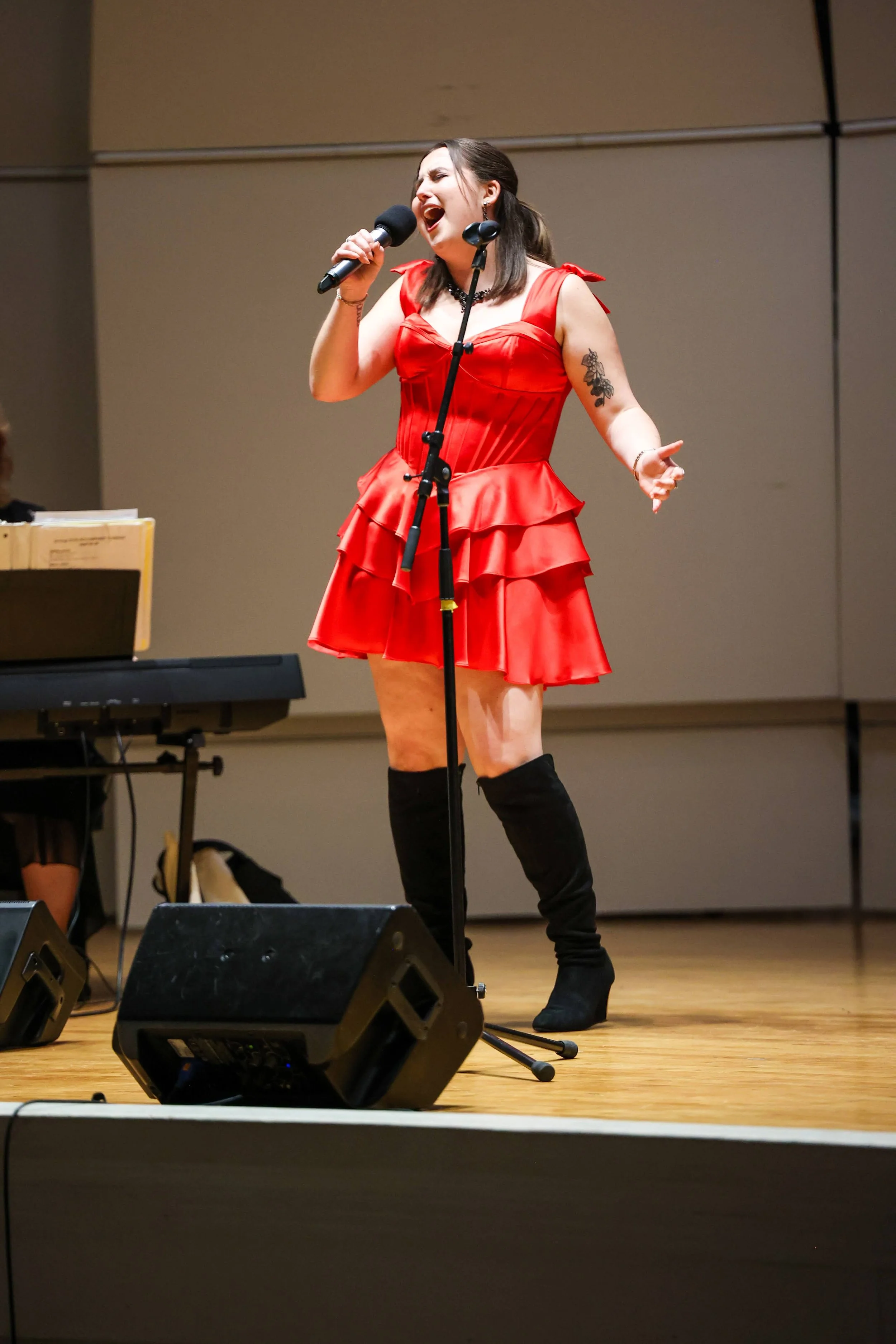 A woman singing on stage in a red ruffled dress and black knee-high boots, holding a microphone.