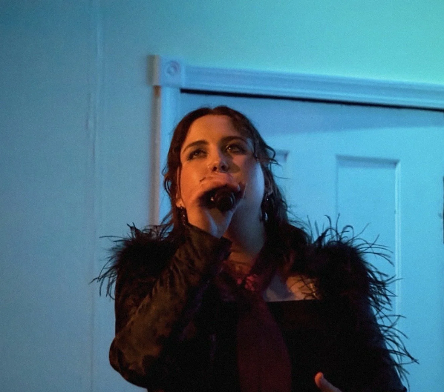 Woman with dark, wavy hair in a black, feathered outfit singing into a microphone against a blue-lit background.