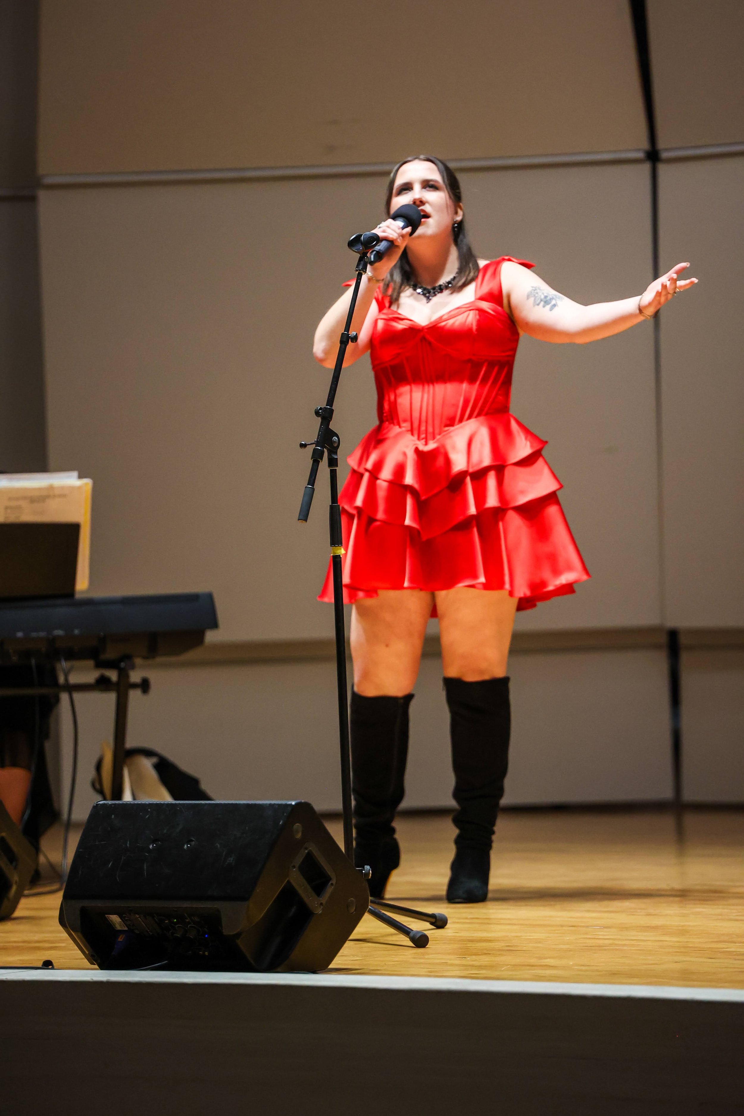 A woman in a red dress singing into a microphone on stage with a keyboard and speaker nearby.