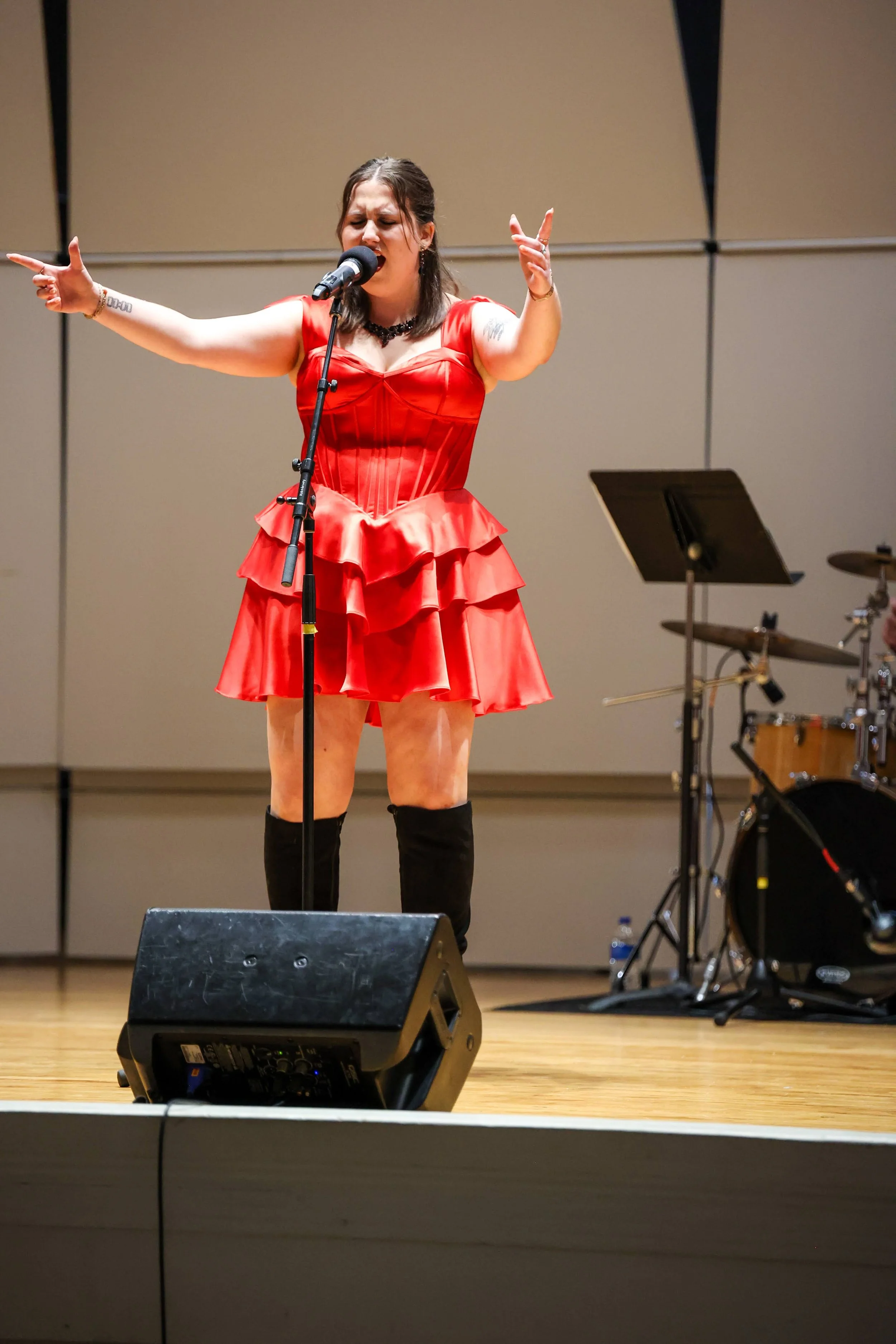 A woman in a red dress singing into a microphone on stage, with musical instruments behind her.