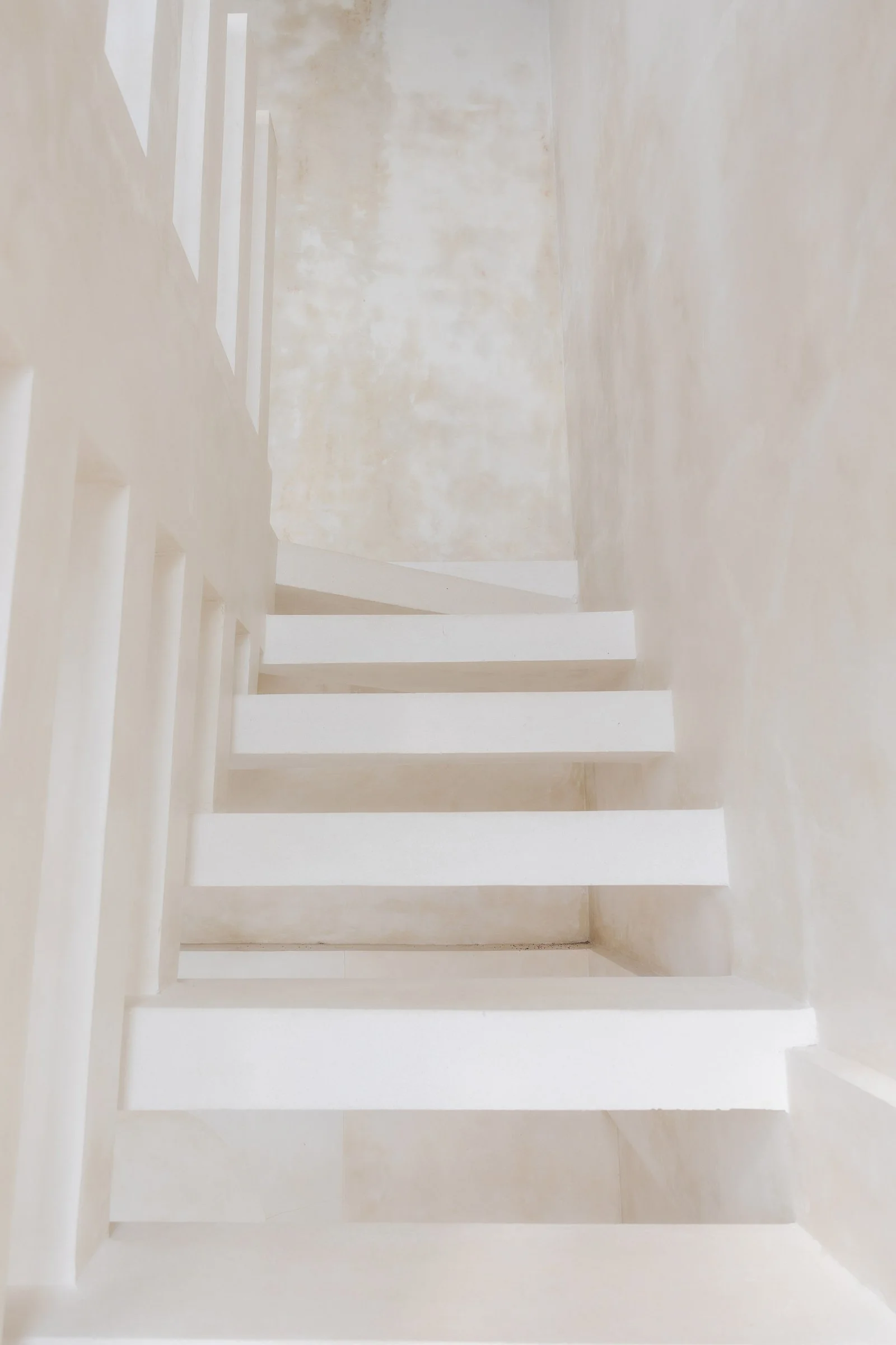 A view of a staircase with white railings and a beige, textured wall in the background.