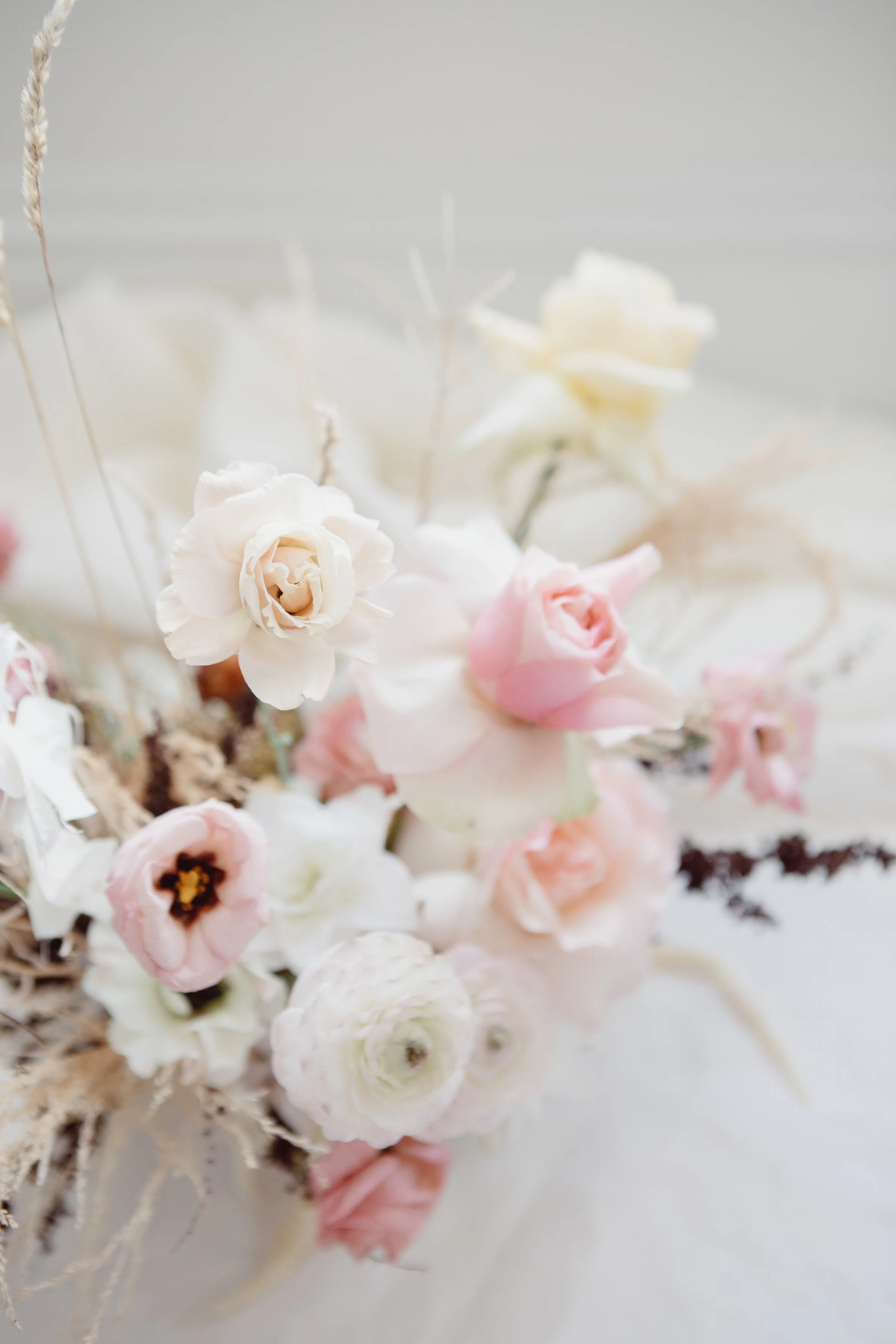 Close-up of a floral arrangement featuring white and pink flowers with soft, delicate petals. The background is neutral and blurred, emphasizing the flowers in the foreground.