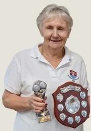 An elderly woman holding a trophy and a shield-shaped plaque with multiple smaller medals inside.