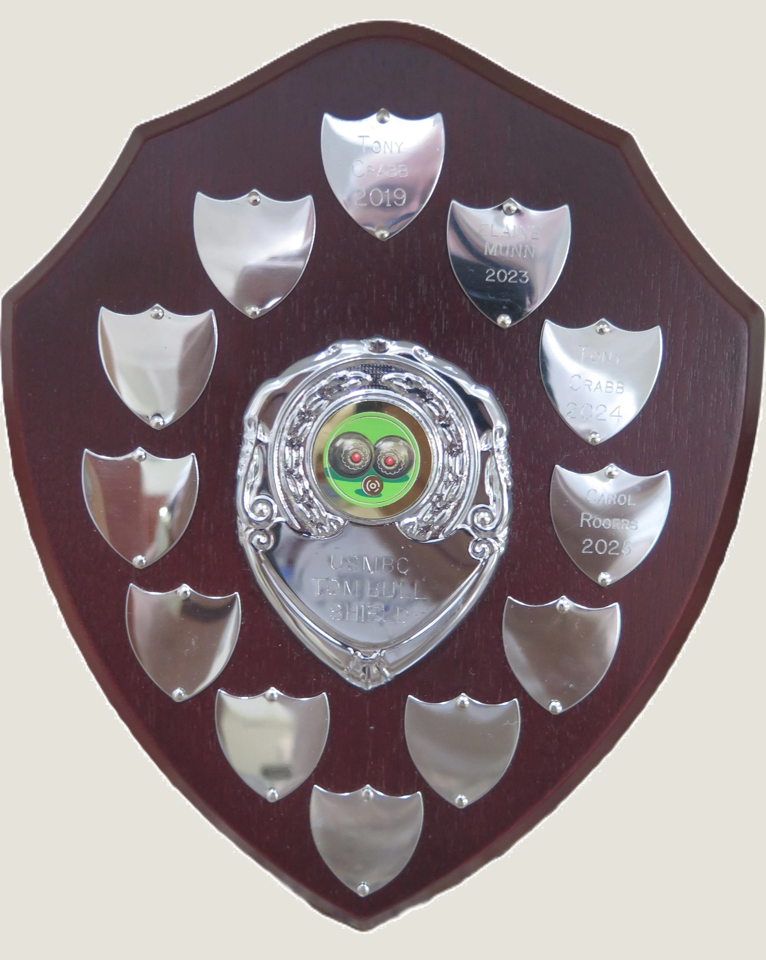 A wooden plaque with metal dog tags engraved with names and years, mounted on it in a decorative pattern.