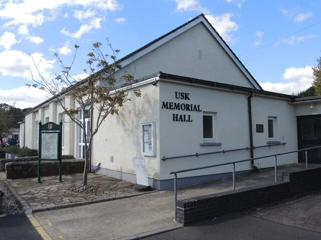 Exterior view of USK Memorial Hall building with a small tree, a signboard, and a ramp for accessibility.