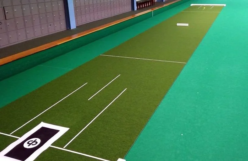 Indoor golf putting practice area with synthetic turf, white lines marking the target zones, and lockers in the background.