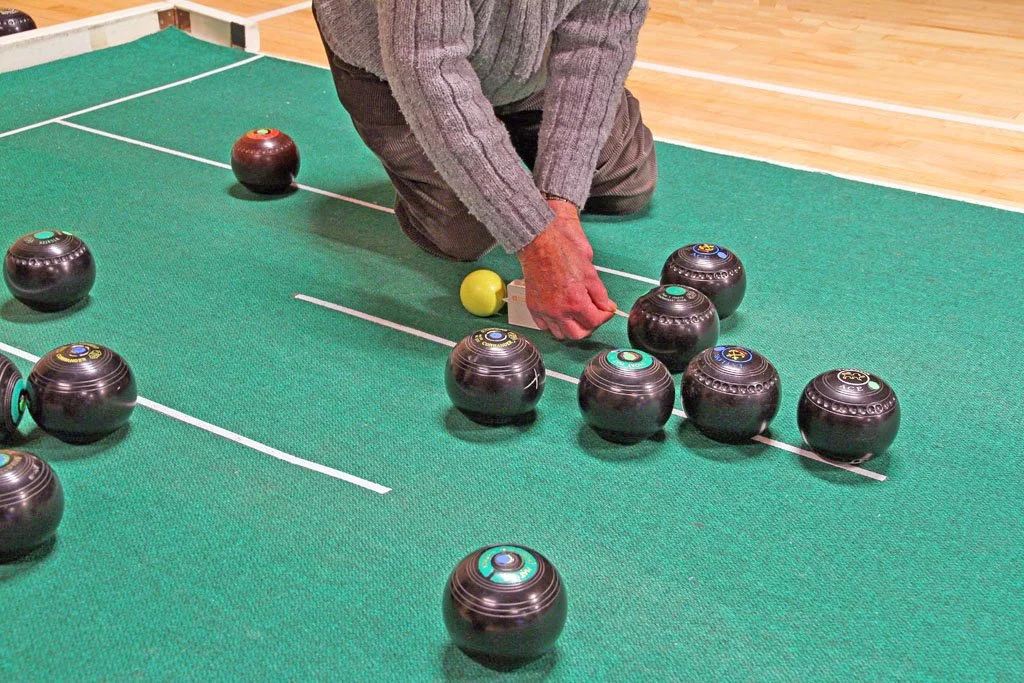 Person arranging black bowls with colored tops and a yellow ball on a green shuffleboard table.