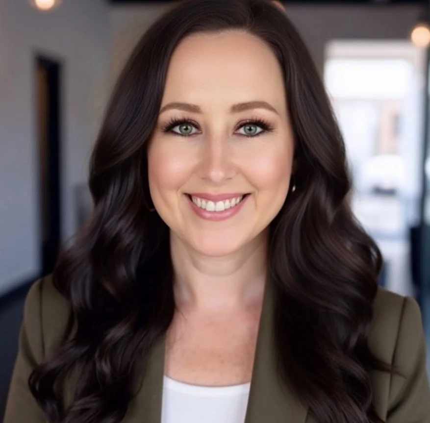 A woman with long, dark brown hair and blue eyes, smiling, in an indoor setting with blurred background.