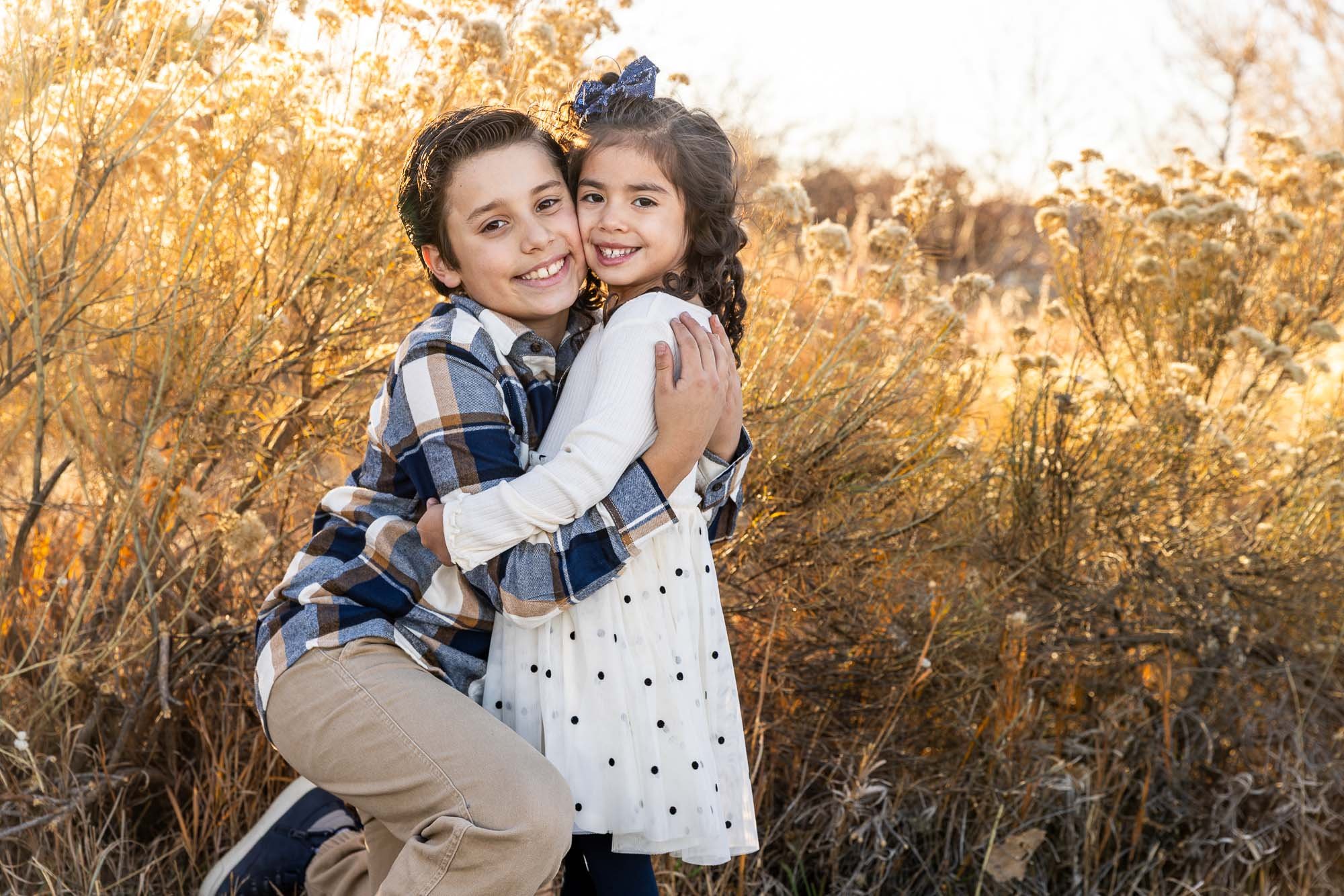 A young boy and girl hugging outdoors during autumn, surrounded by golden foliage.