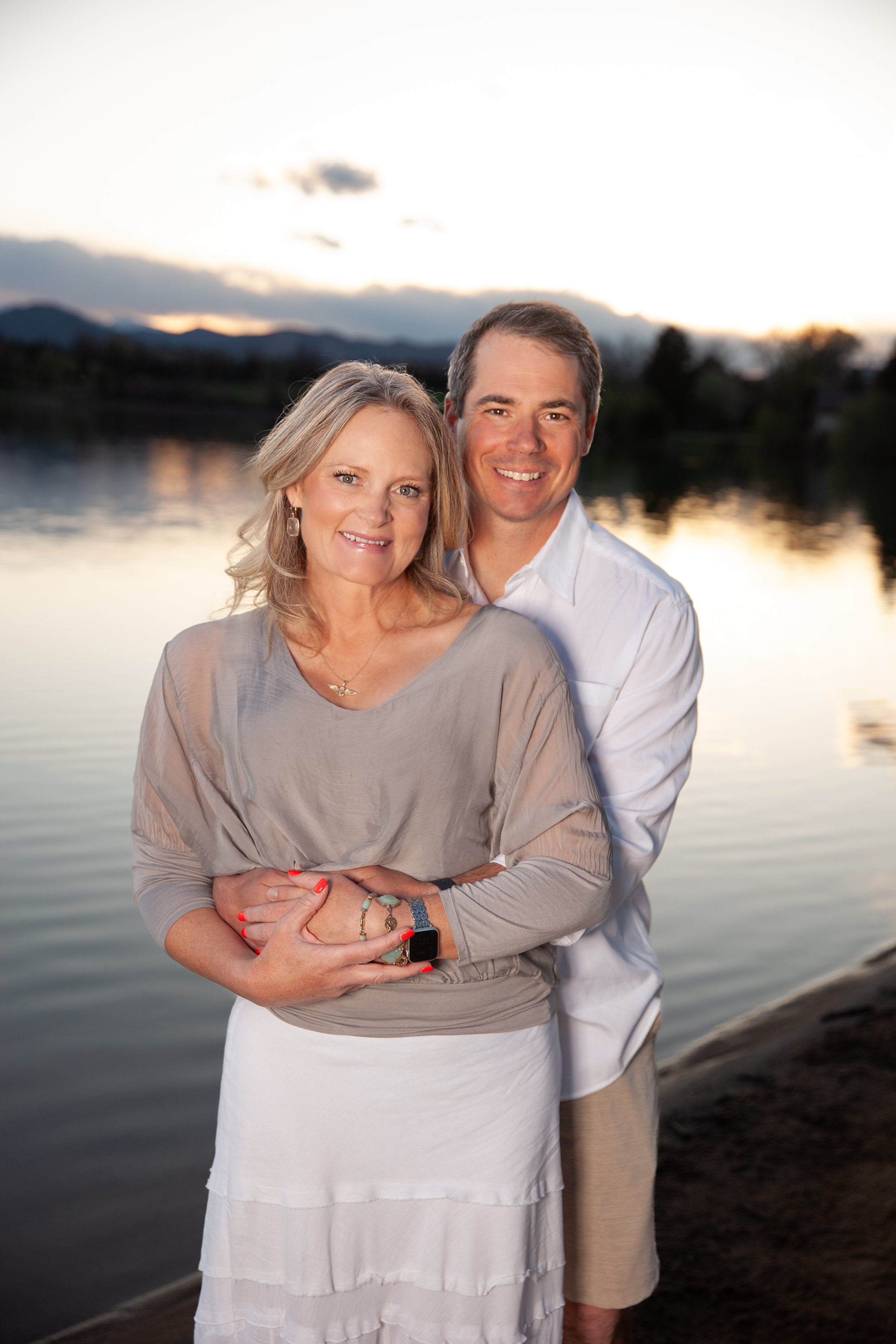 A couple embracing by a lake at sunset.