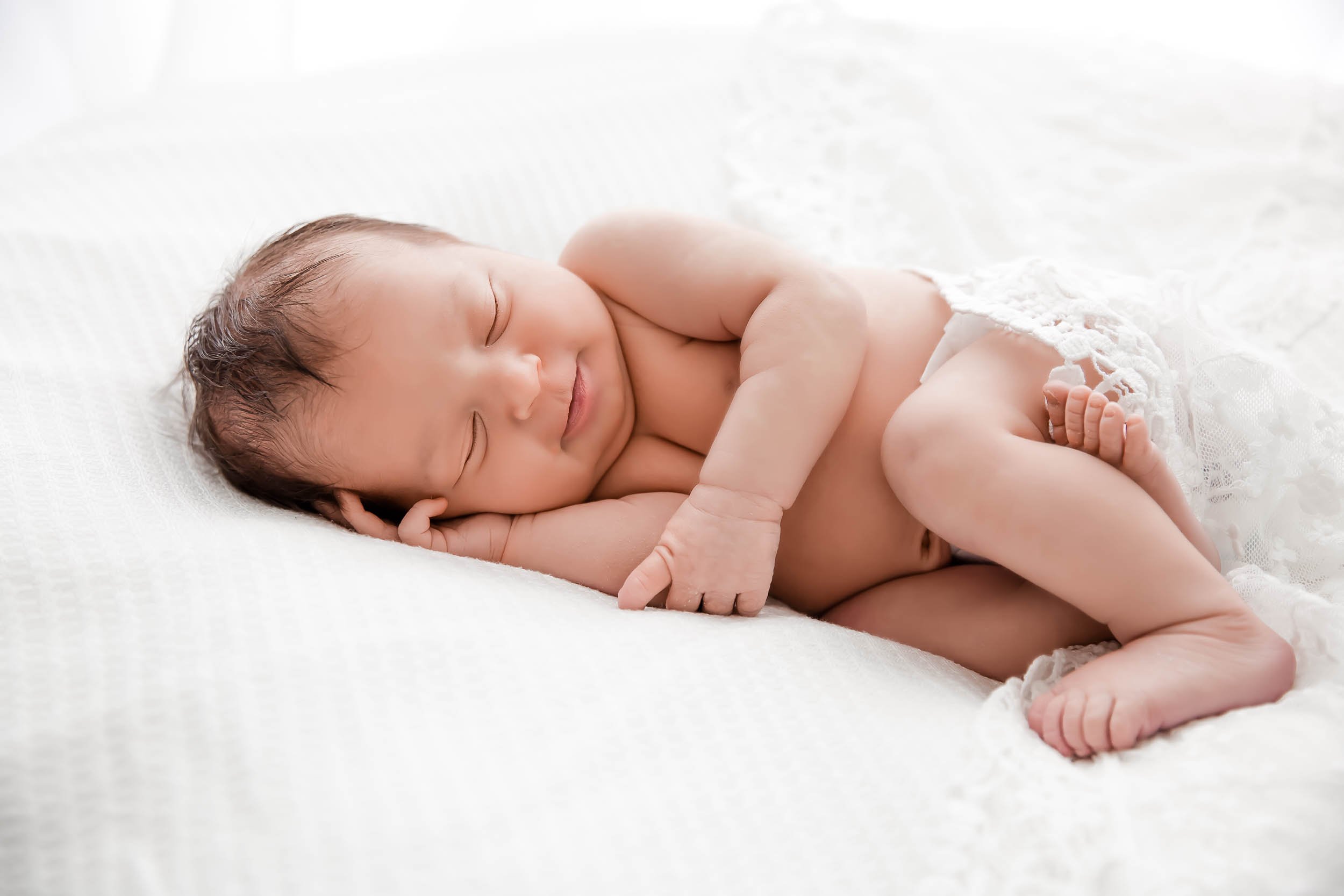 Photo of a sleeping newborn lightly wrapped in a lace cloth