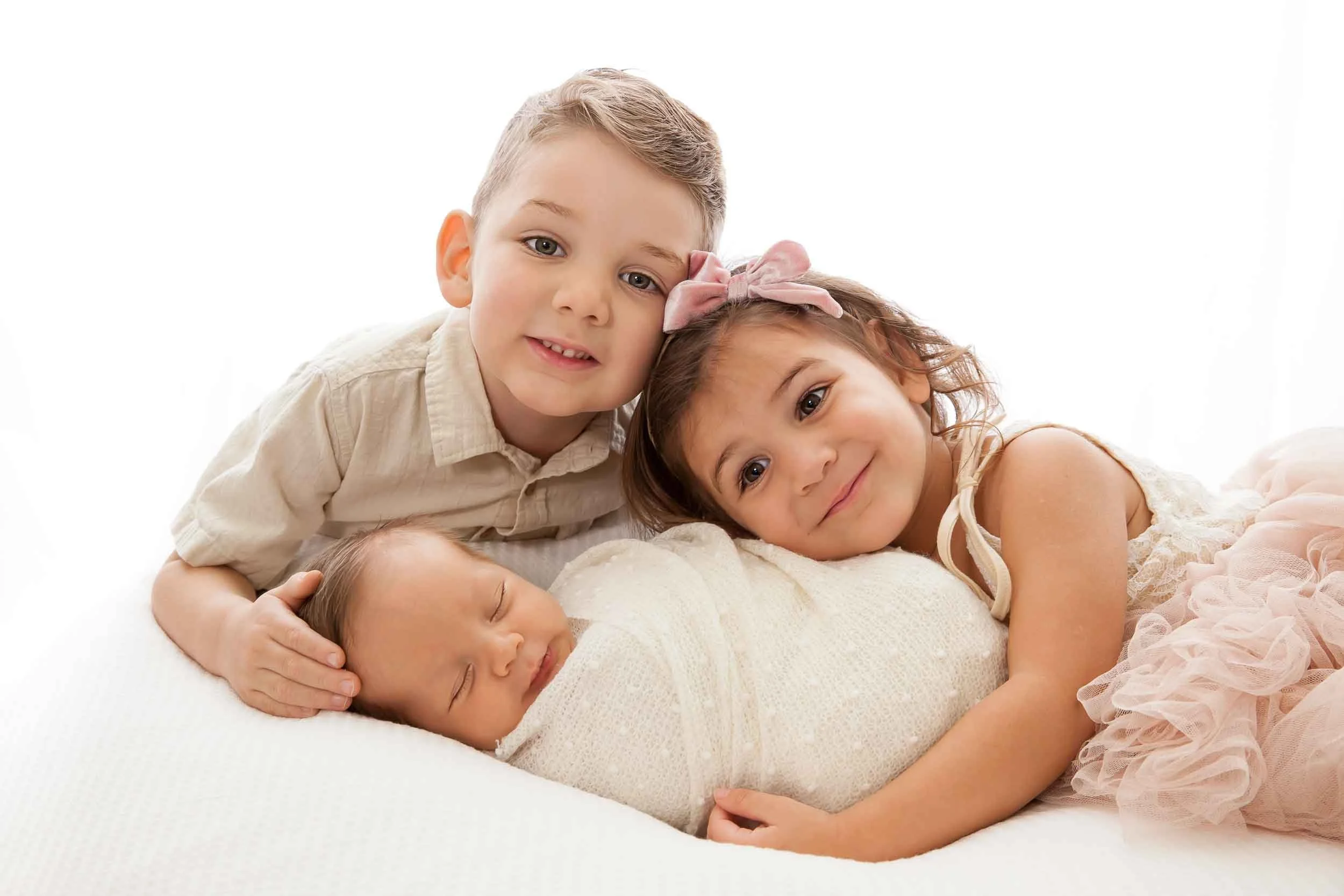 Three children resting on a soft surface, with one sleeping and the others awake, in a bright setting with a white background.