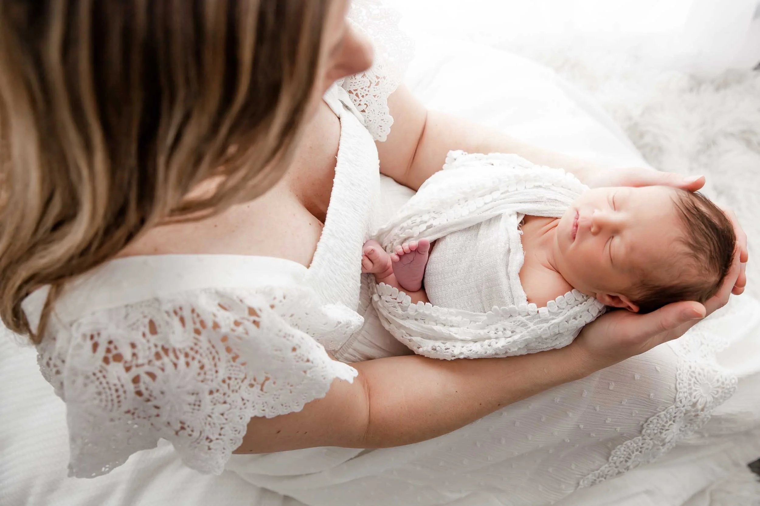 Photo of a newborn baby wrapped in lace and held in the arms of her mother