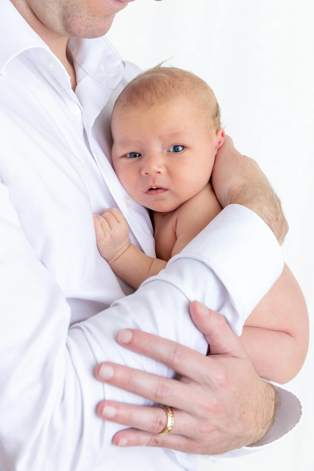 A man in a white shirt holding a baby with blond hair and blue eyes against a white background.