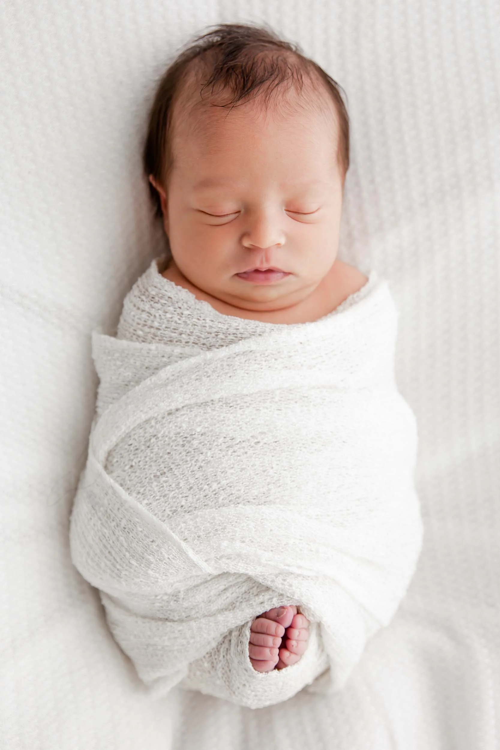 Photo of a newborn baby wrapped in a white cloth with toes peeking out