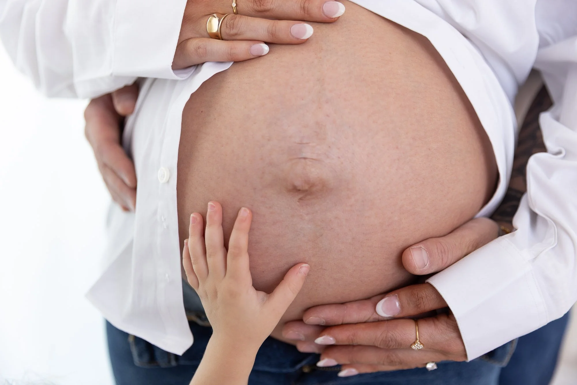  Pregnant woman with her belly exposed, holding her abdomen as a child gently touches her belly.