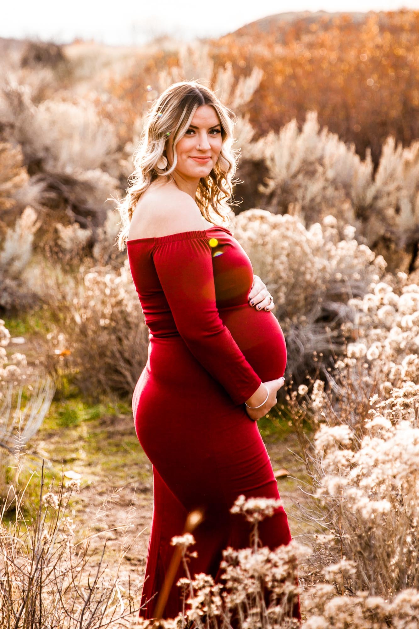 Pregnant woman in a red dress standing in field with dry grasses.