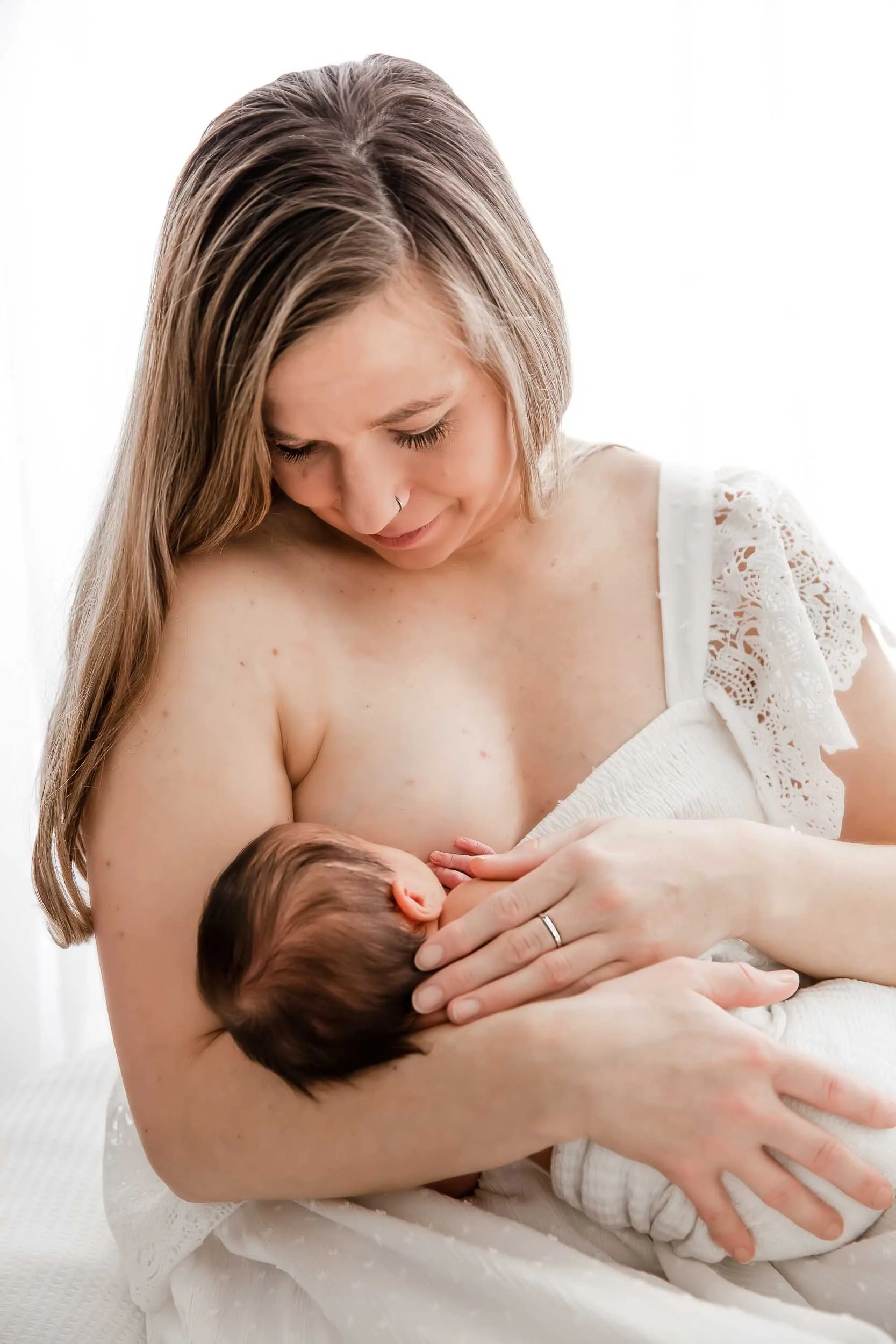 Photo of a blonde mother breastfeeding her newborn and gazing down at her. 
